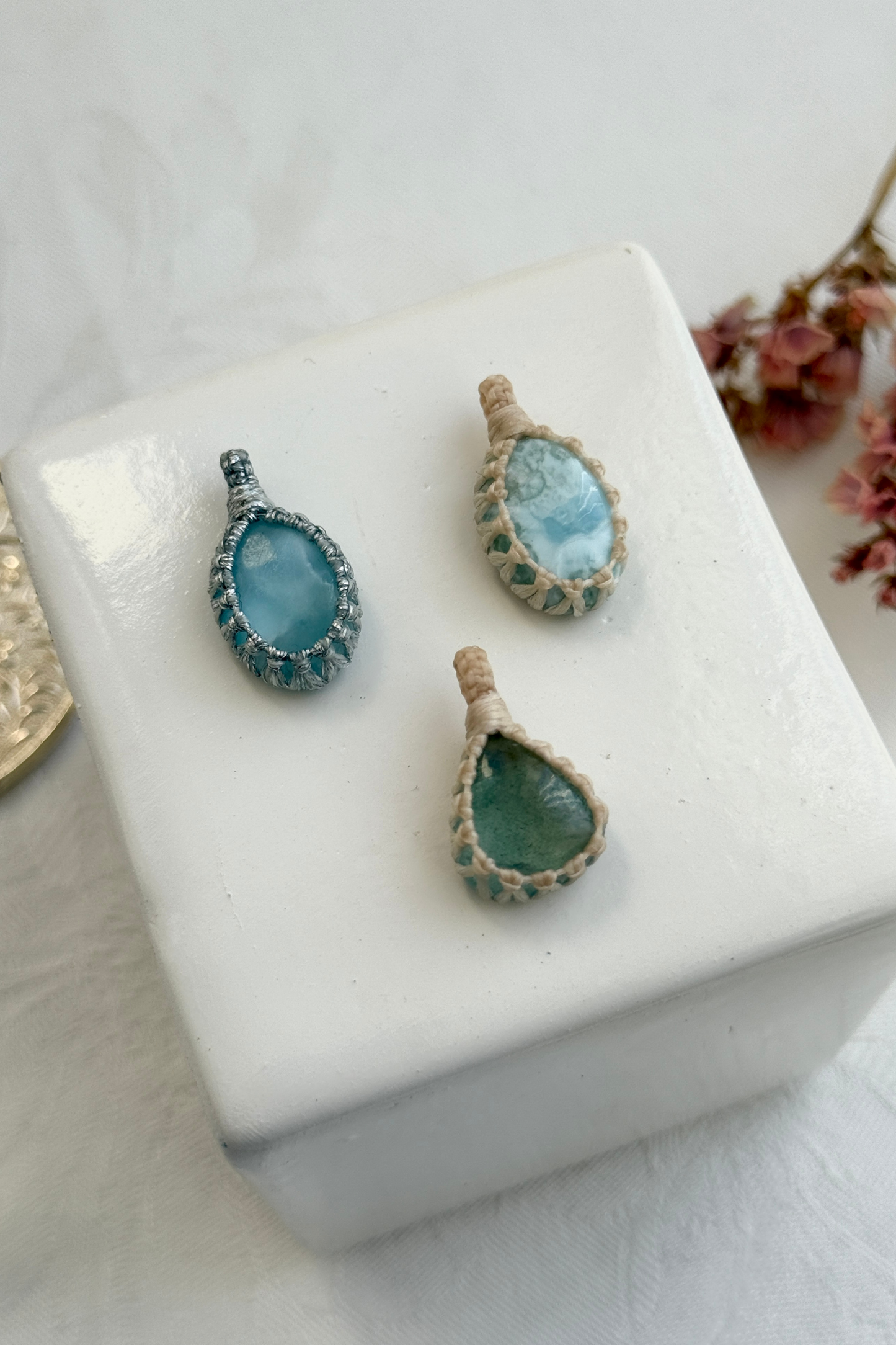 Close-up view of handmade Candy Charms with natural Larimar and Aquamarine gemstone pendants, showcasing the macrame wrapping and unique stone details.