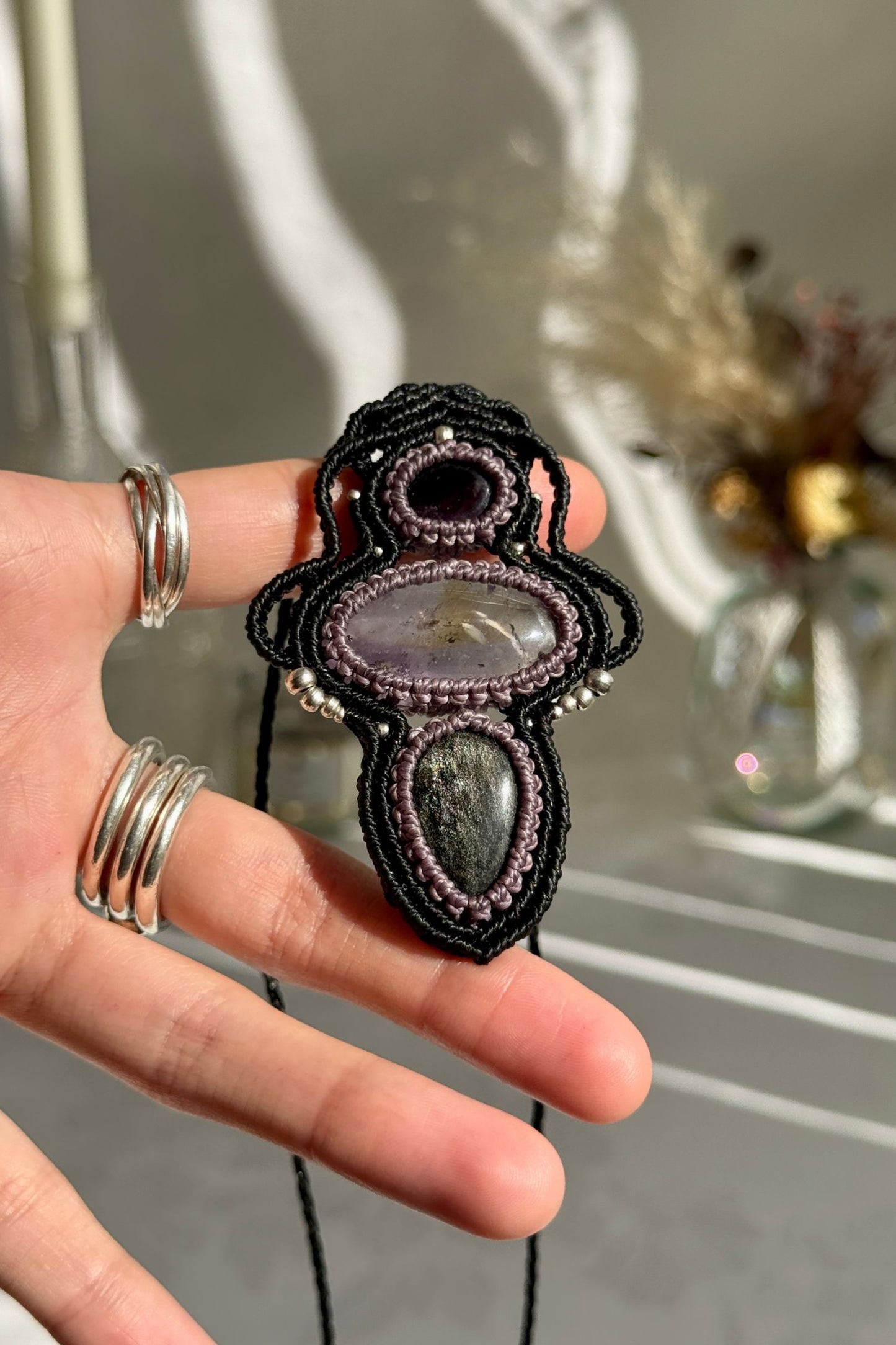 Hand holding a handmade Amethyst, Ametrine and Silver Sheen Obsidian necklace, highlighting the intricate macrame work and the natural glow of the gemstones.