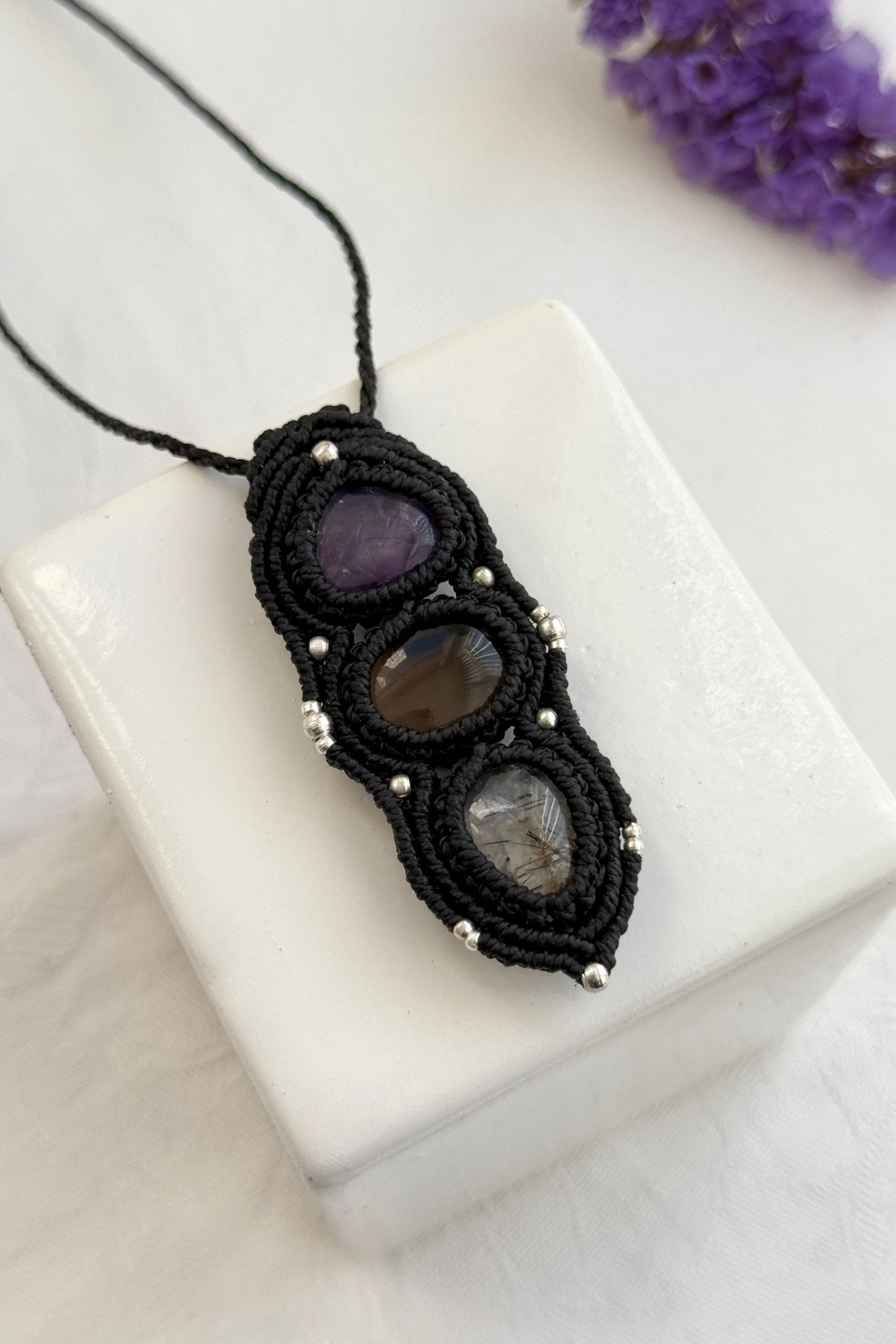 Detailed close-up of Amethyst, Smoky Quartz and Tourmaline Quartz gemstones in a handmade macrame necklace. Showcasing natural textures and gemstone glow.