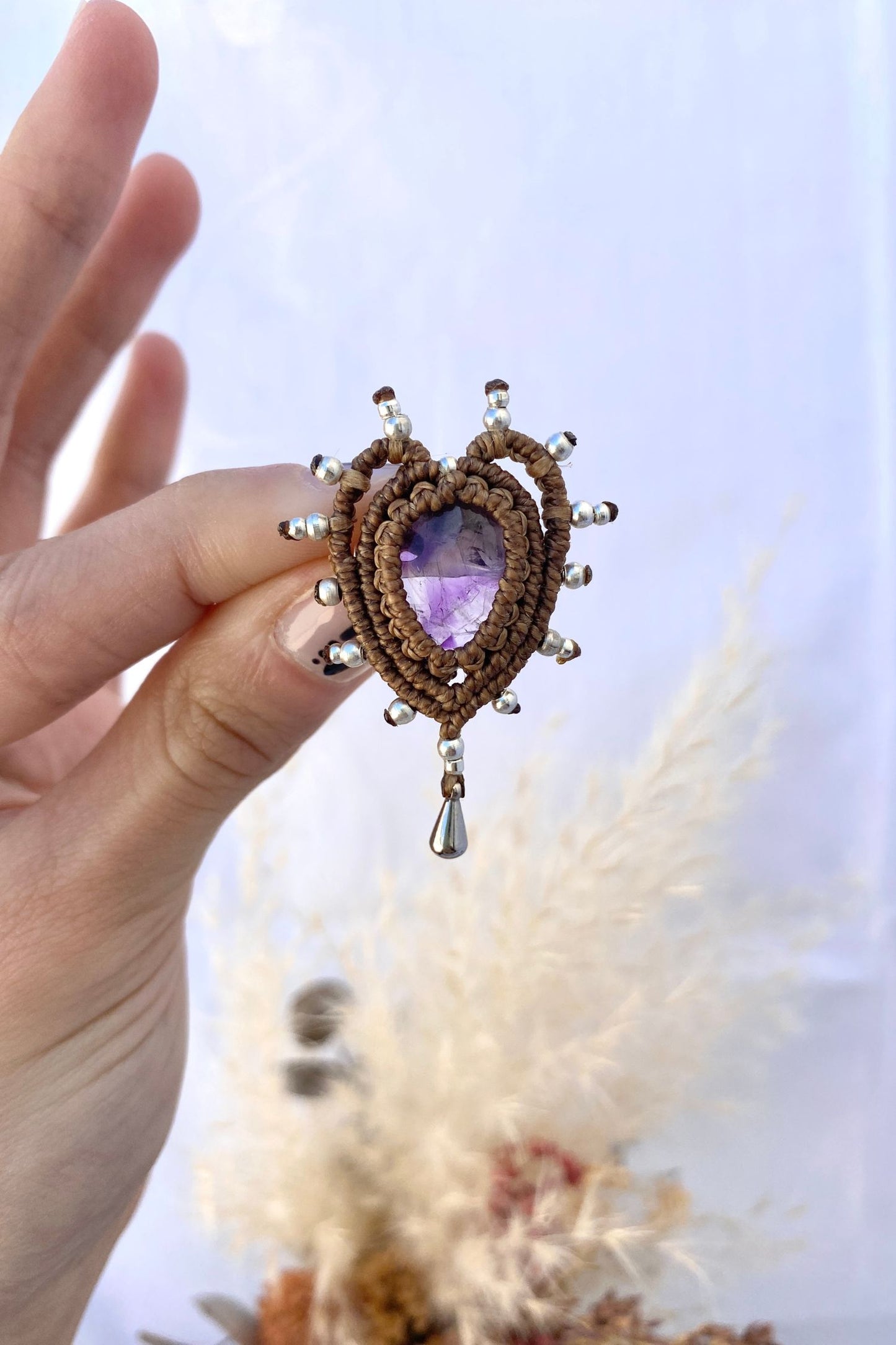 Handmade heart-shaped brooch featuring a natural amethyst gemstone at the center, intricately crafted with macrame and a delicate drop detail.