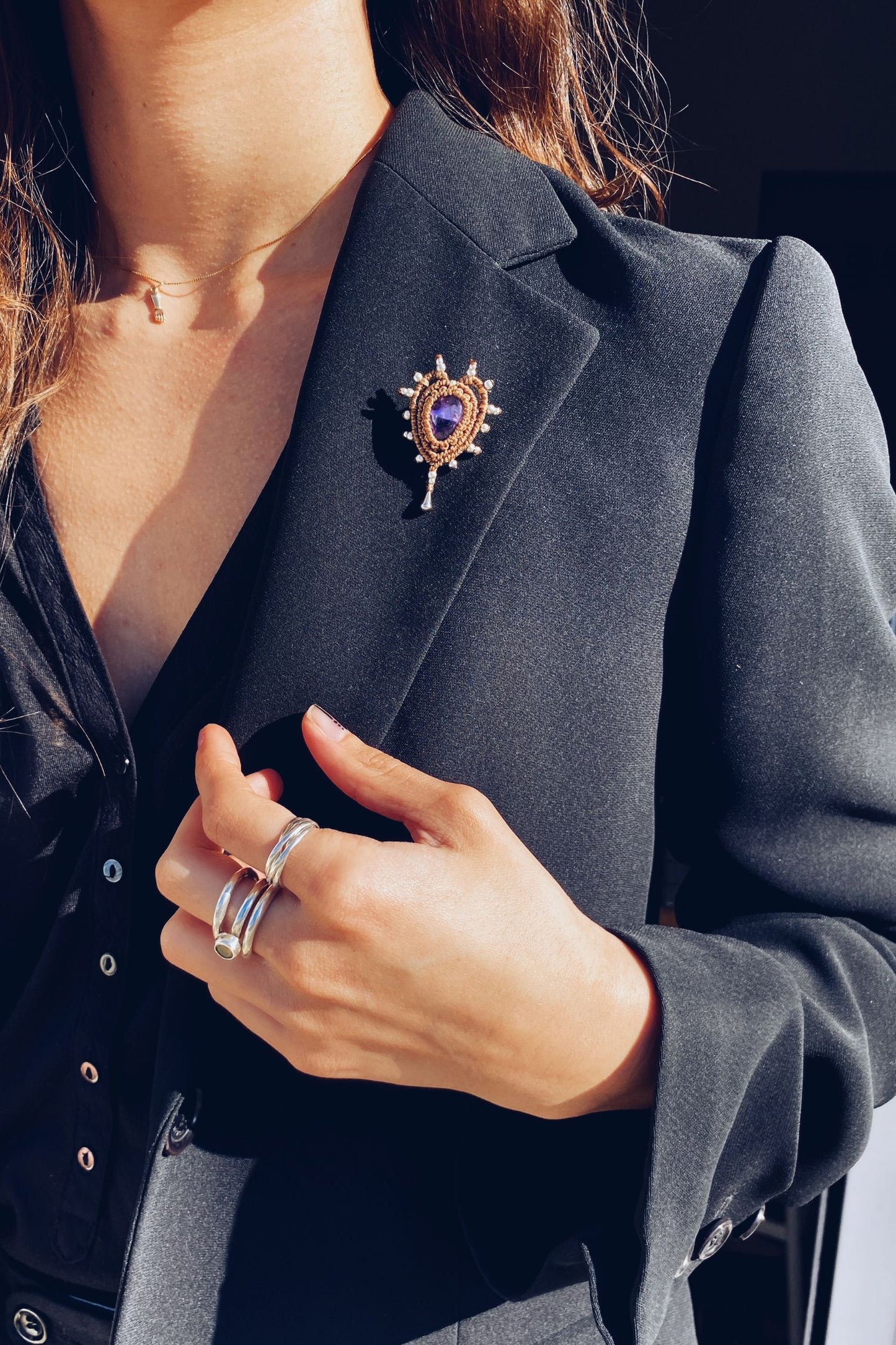 Cupid Amethyst Brooch, a handmade heart-shaped macrame pin with a deep purple amethyst, styled on a black blazer for an elegant statement look.