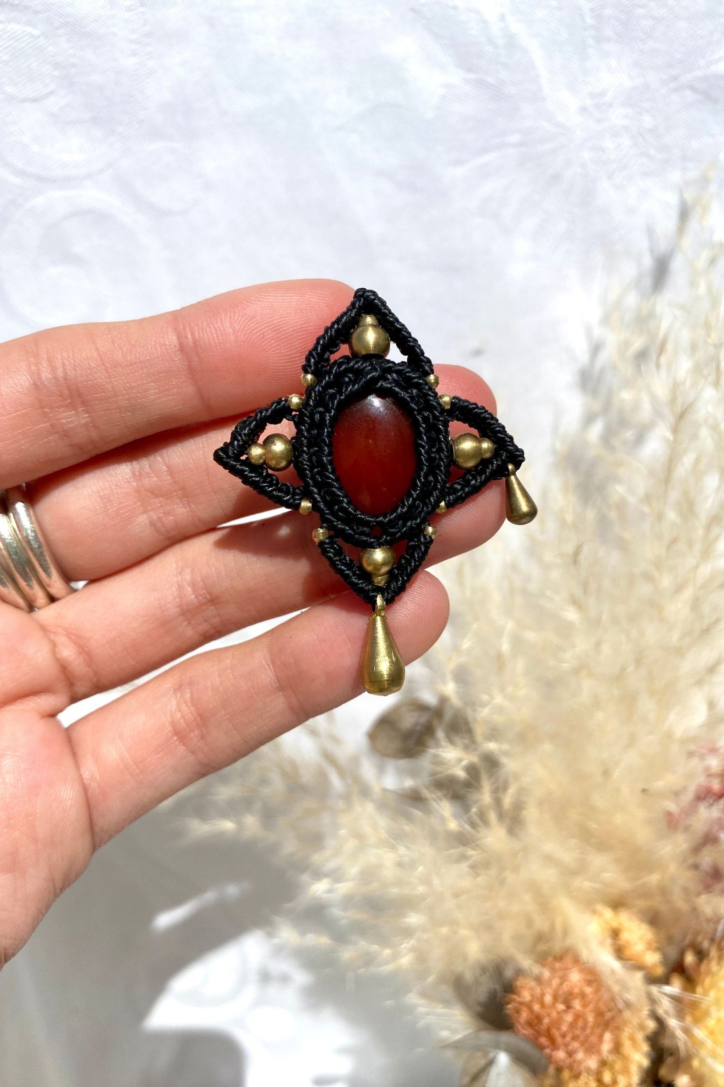 Handmade statement brooch with a deep red Carnelian gemstone and asymmetrical golden details, held in hand to showcase its size and intricate design.
