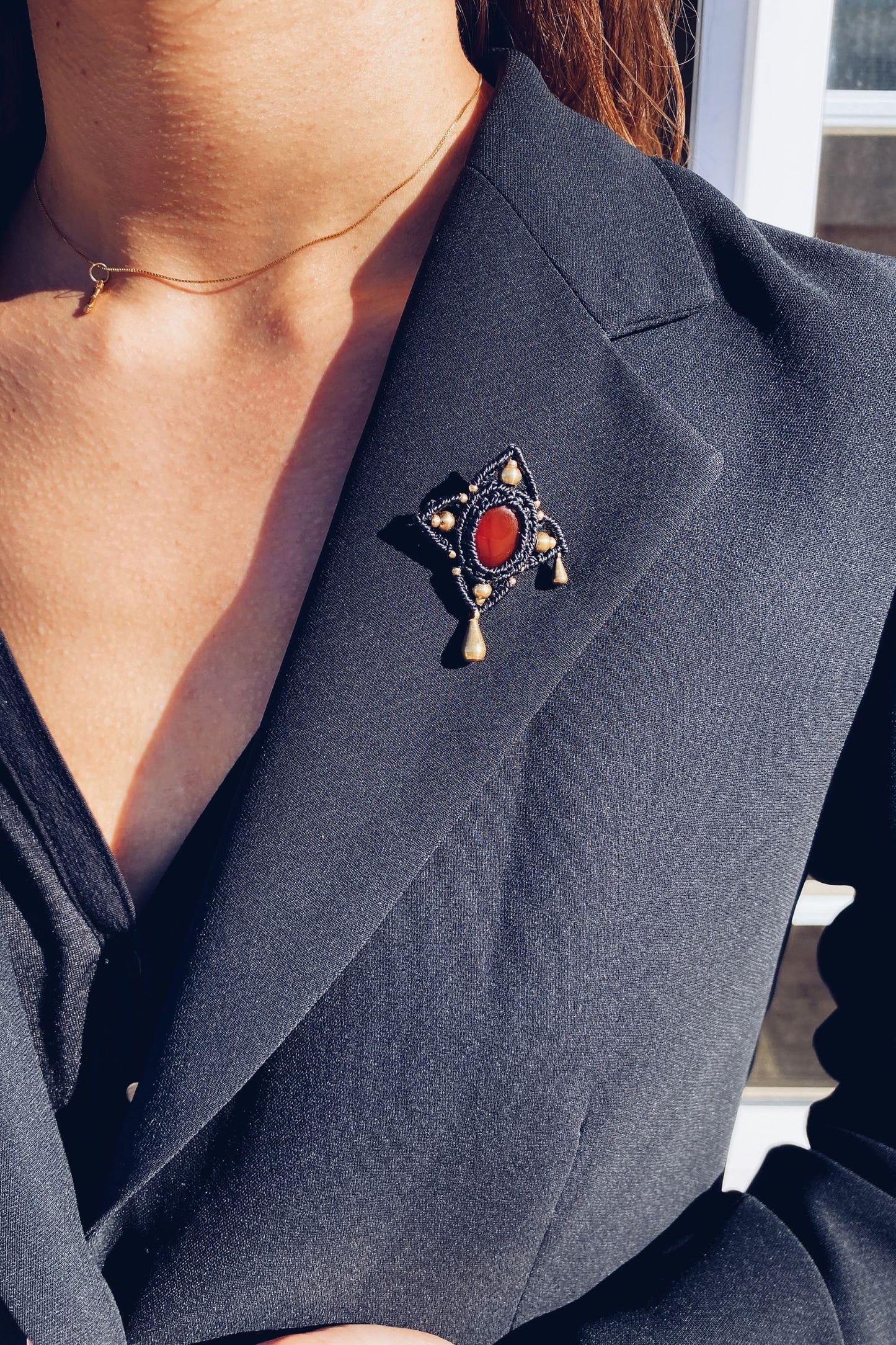 Handmade statement brooch featuring a bold red Carnelian gemstone at the center, with asymmetrical golden drops, styled on a lapel to showcase its elegant and eye-catching design. A versatile accessory that elevates any look.