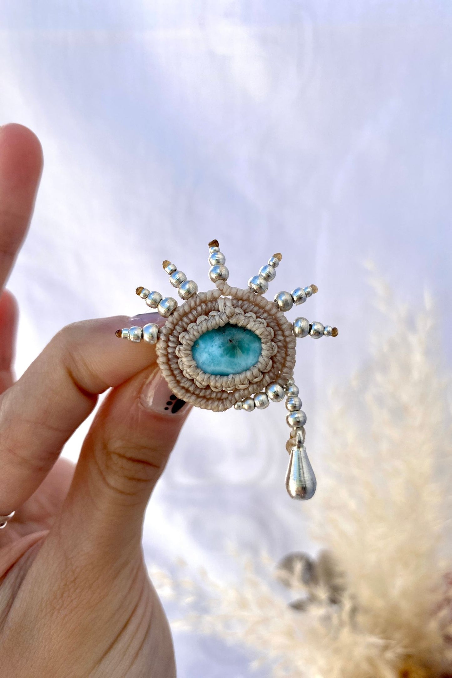 Handmade statement brooch featuring a stunning blue Larimar gemstone at the center, with silver beads forming a high-dropping teardrop design. A unique and artistic jewelry piece.