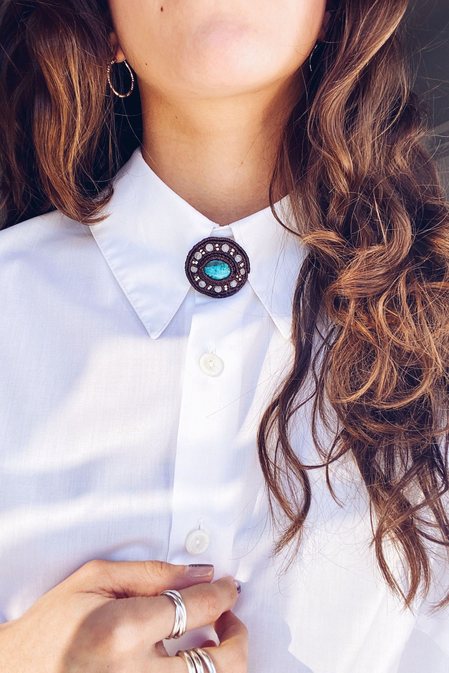 Handmade round macrame brooch featuring a vibrant turquoise gemstone at the center, accented with delicate moonstone beads. Styled on a white shirt for a boho-inspired look.