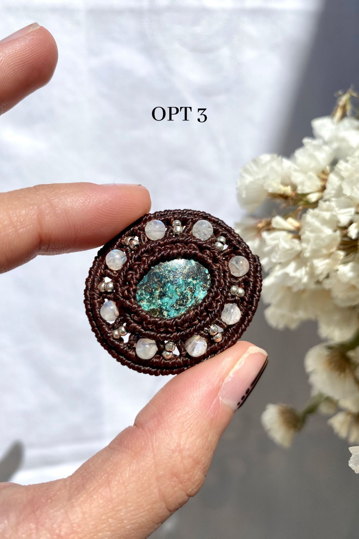 Handmade round turquoise brooch being secured in hand, showing its detailed craftsmanship and elegant macrame design.