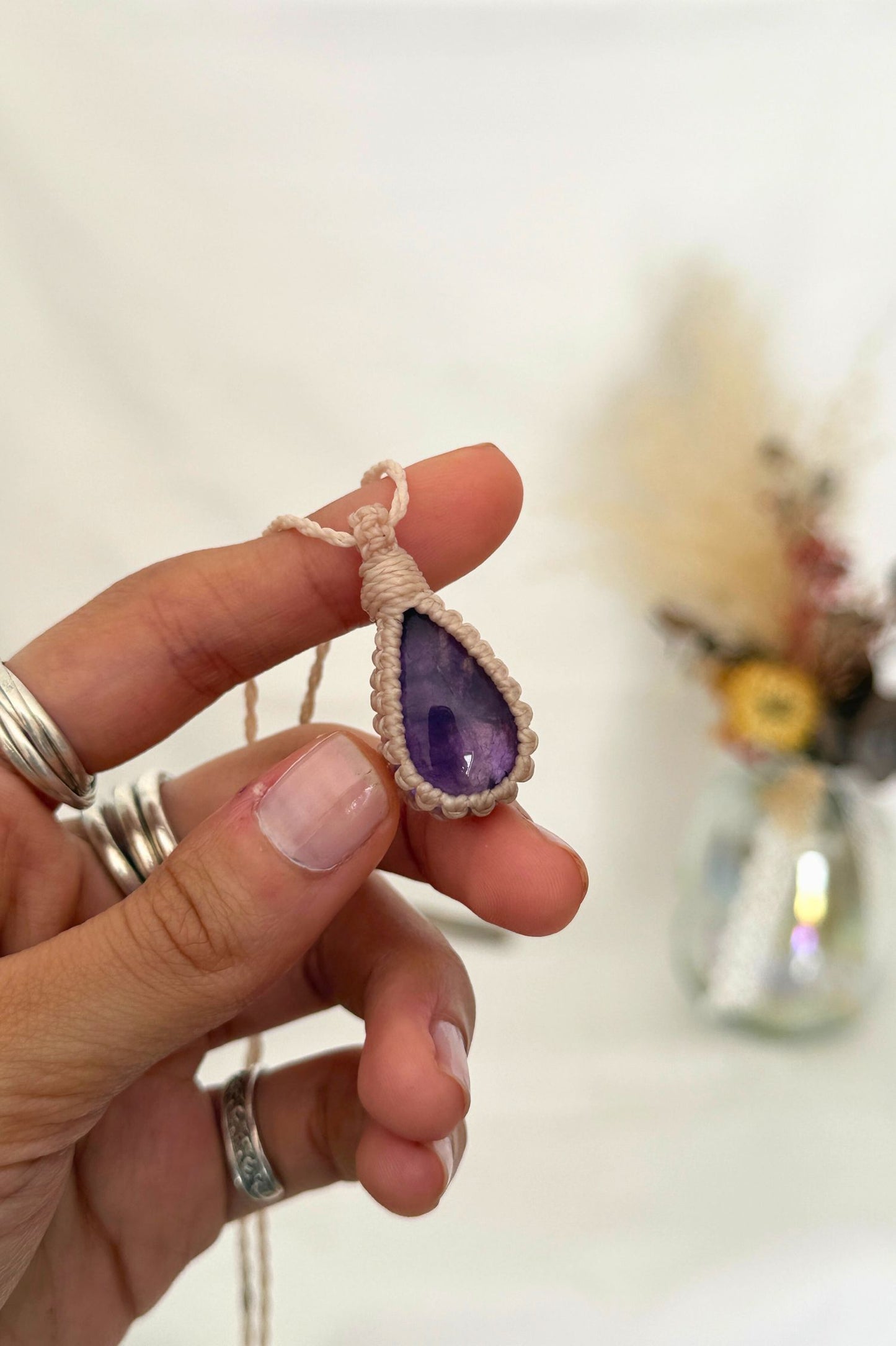 Close-up of handmade Amethyst Macrame necklace in hand, showcasing the intricate macrame knotting and the vibrant color of the gemstone.