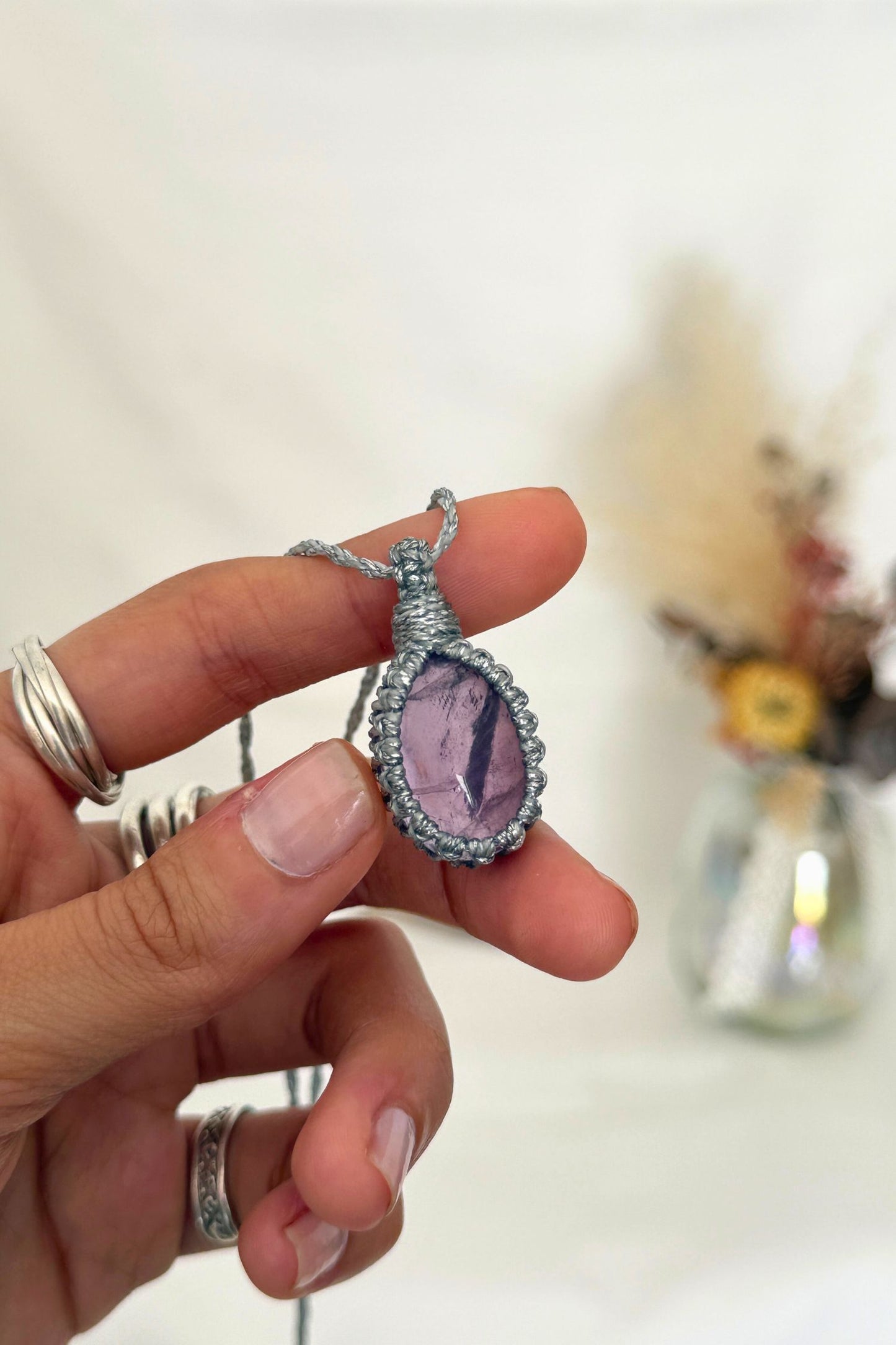 Close-up of handmade Amethyst Macrame necklace in hand, showcasing the intricate macrame knotting and the vibrant color of the gemstone.