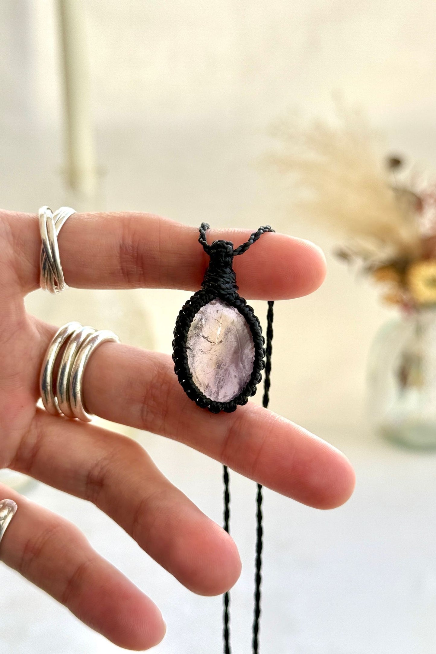 Hand holding a handmade Ametrine macrame necklace with a black cord, showcasing the gemstone's harmonious blend of soft purple Amethyst hues and the mysterious golden glow of Citrine.