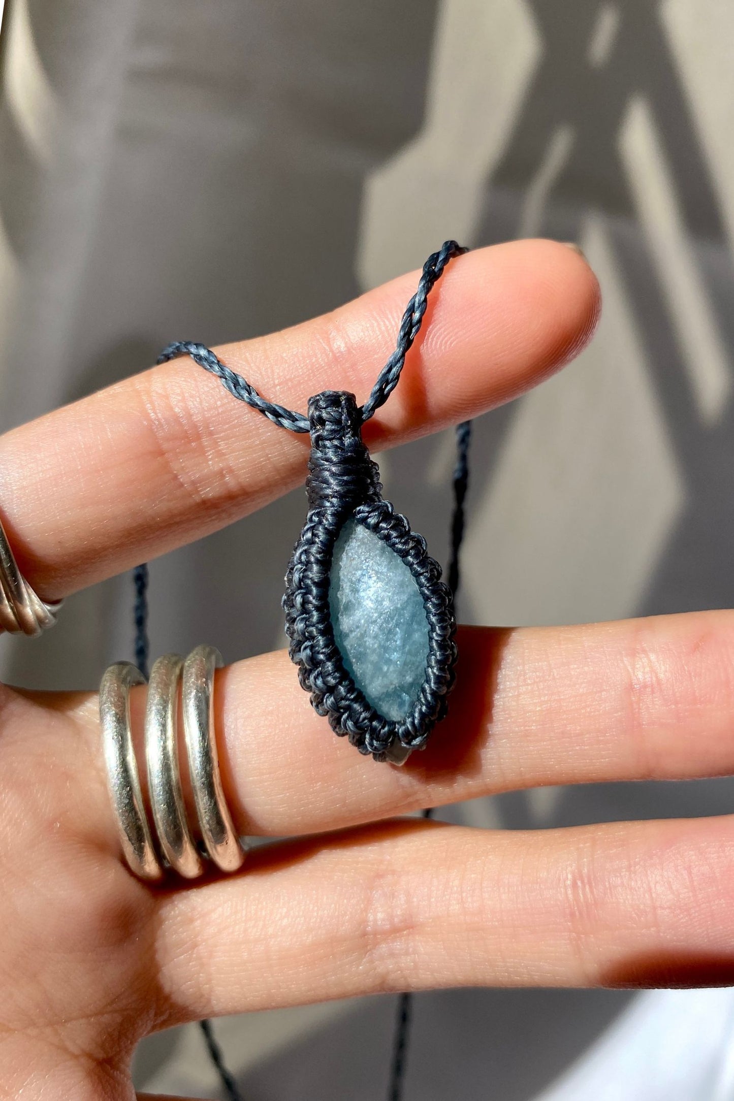 Hand holding a handmade Aquamarine Macrame necklace from the Essence collection, featuring a high-quality blue gemstone in a delicate everyday-wear design.