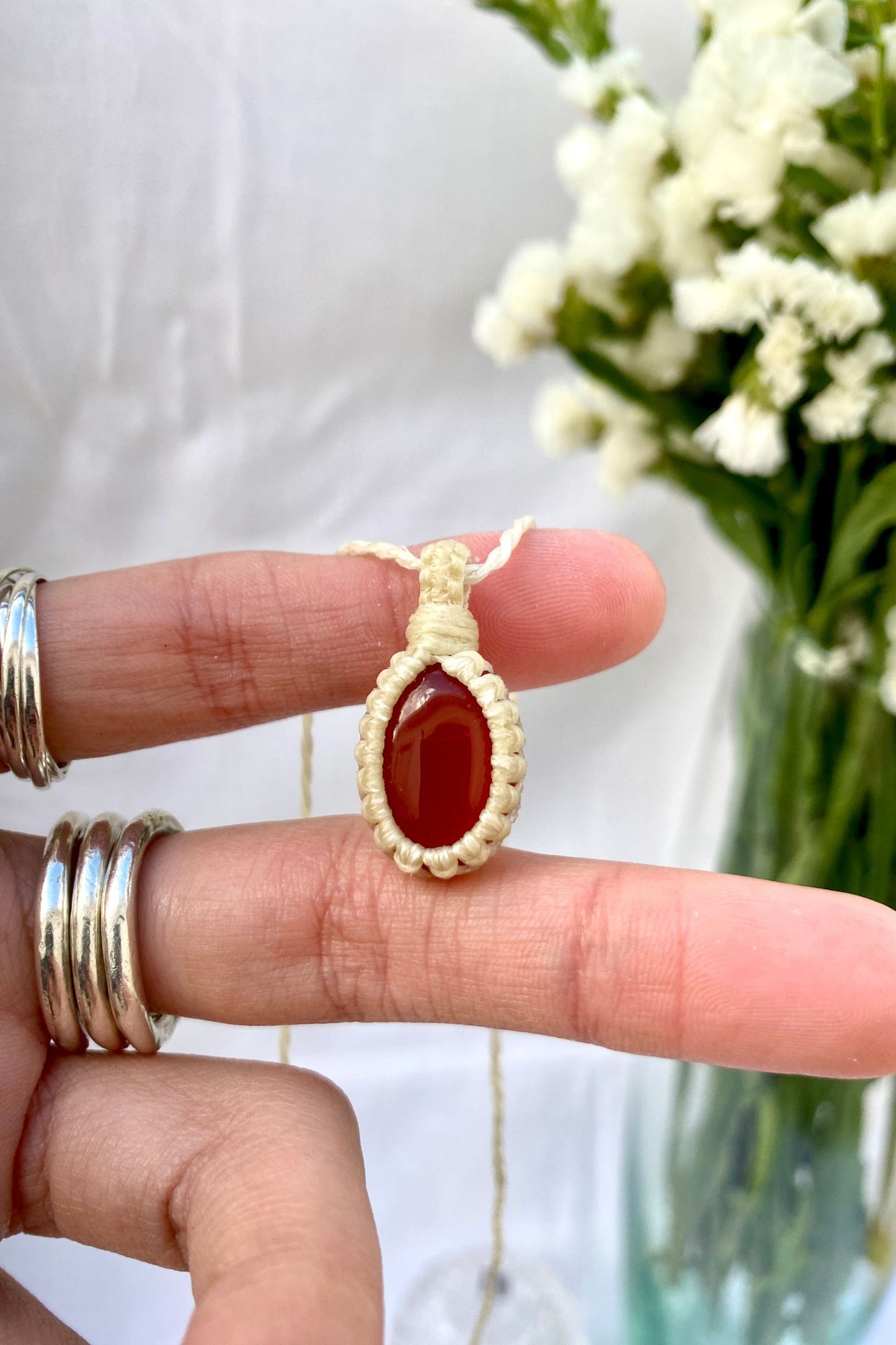 Hand holding a handmade Carnelian macrame necklace, showcasing the gemstone’s rich red hue and smooth polished surface.
