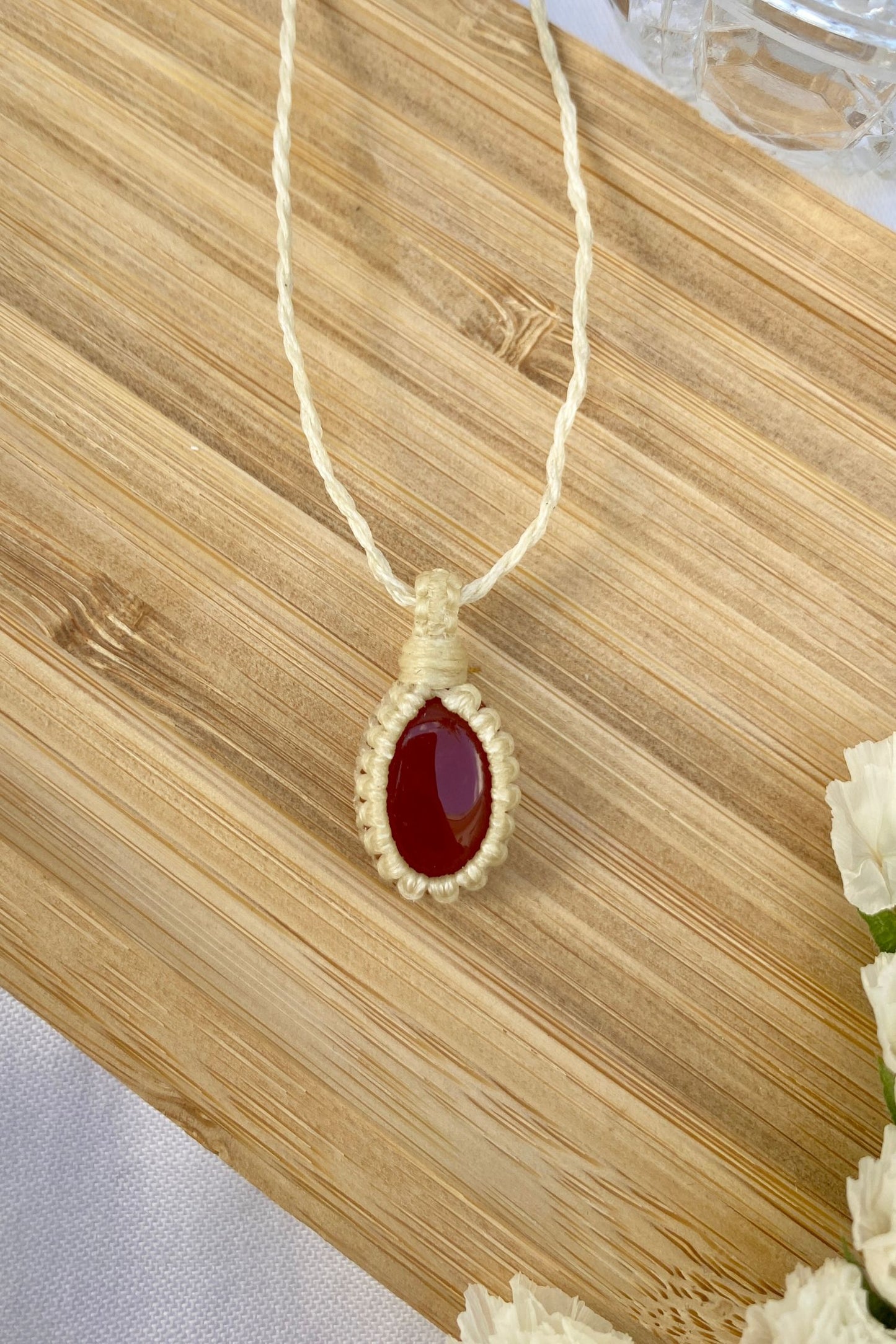 Delicate handmade Carnelian macrame necklace laid flat, featuring a bold red gemstone wrapped in fine macrame knotting.