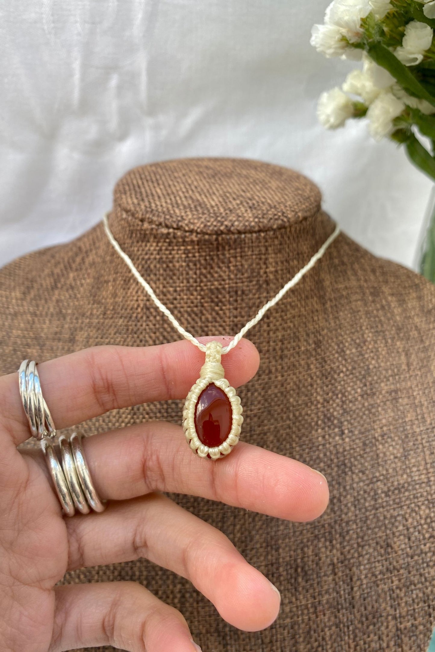 Close-up of a handmade Carnelian macrame necklace on a display stand, with a hand holding the piece to showcase its fine details and craftsmanship.