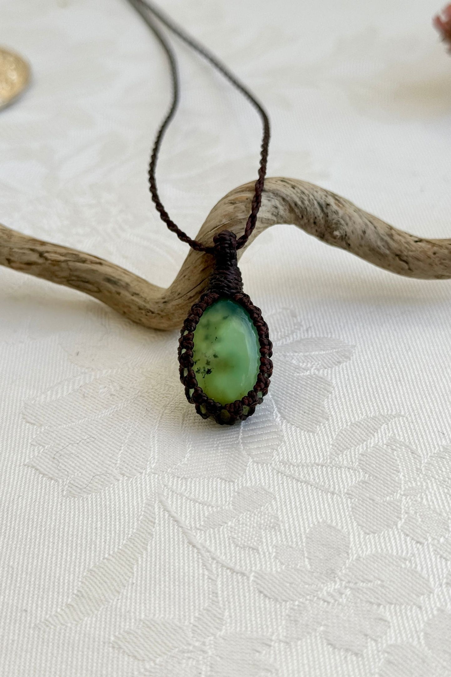 Handmade Chrysoprase macrame necklace with a brown cord, laid flat to display its intricate design and glowing gemstone.