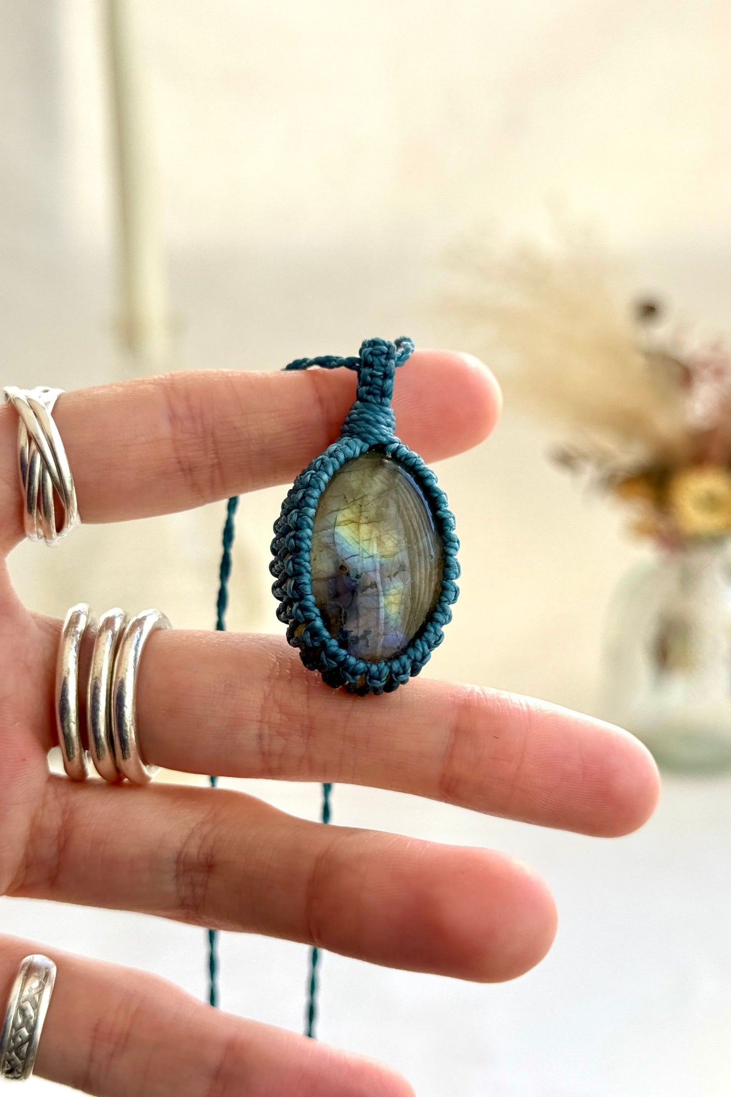 Hand holding a handmade Labradorite macrame necklace with a blue cord, showcasing the gemstone's shimmers with deep blue flashes and subtle golden highlights.