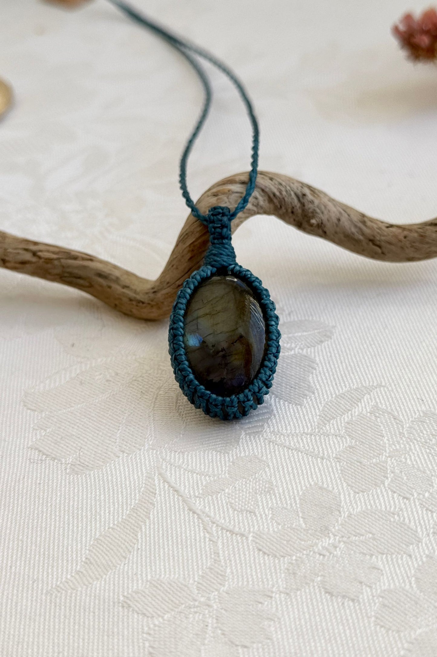 Handmade Labradorite macrame necklace with a blue cord, laid flat to display its intricate design and glowing gemstone.