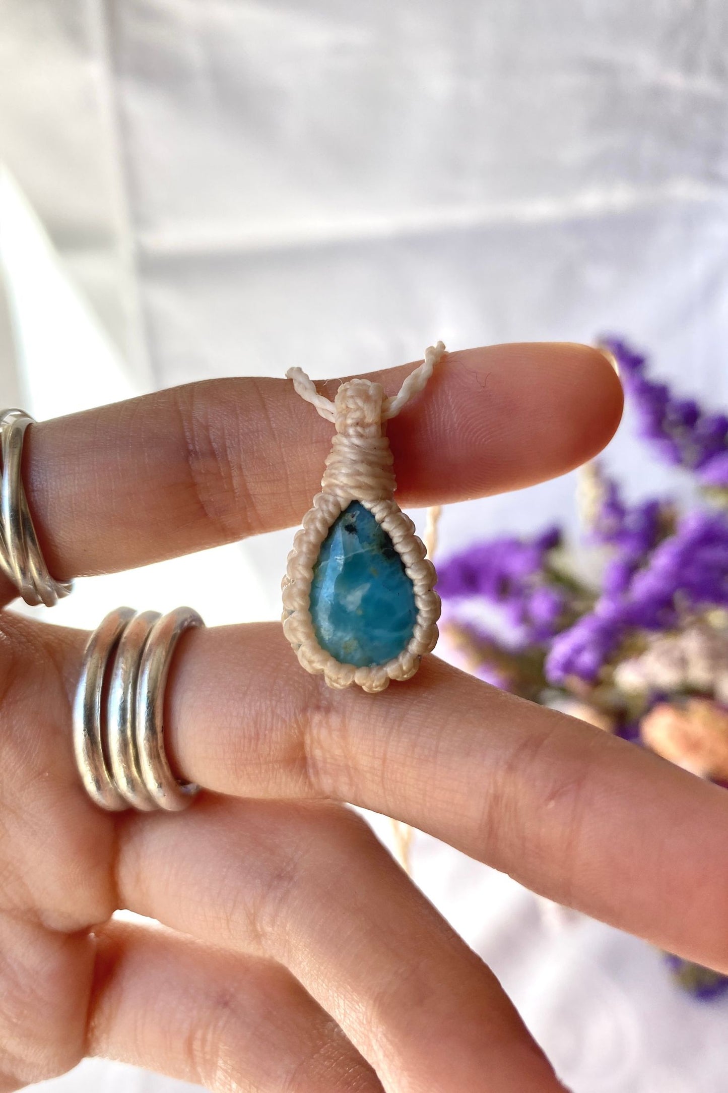 Close-up of handmade Larimar Macrame necklace in hand, showcasing the intricate macrame knotting and the vibrant blue hues of the gemstone.