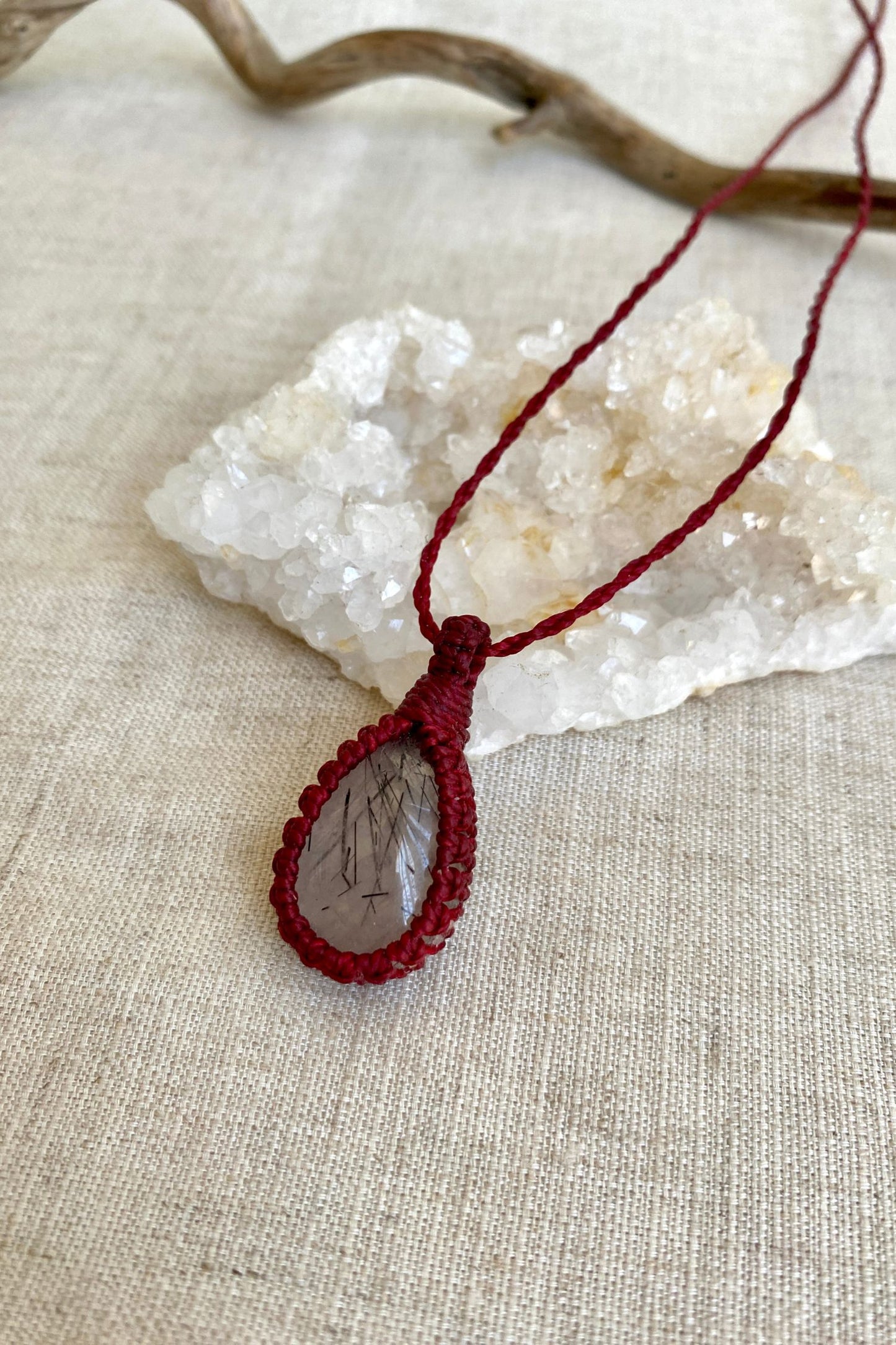 Side-angle view of a handmade Tourmaline Quartz macrame necklace, showcasing the red macrame cord and the gemstone’s unique inclusions.