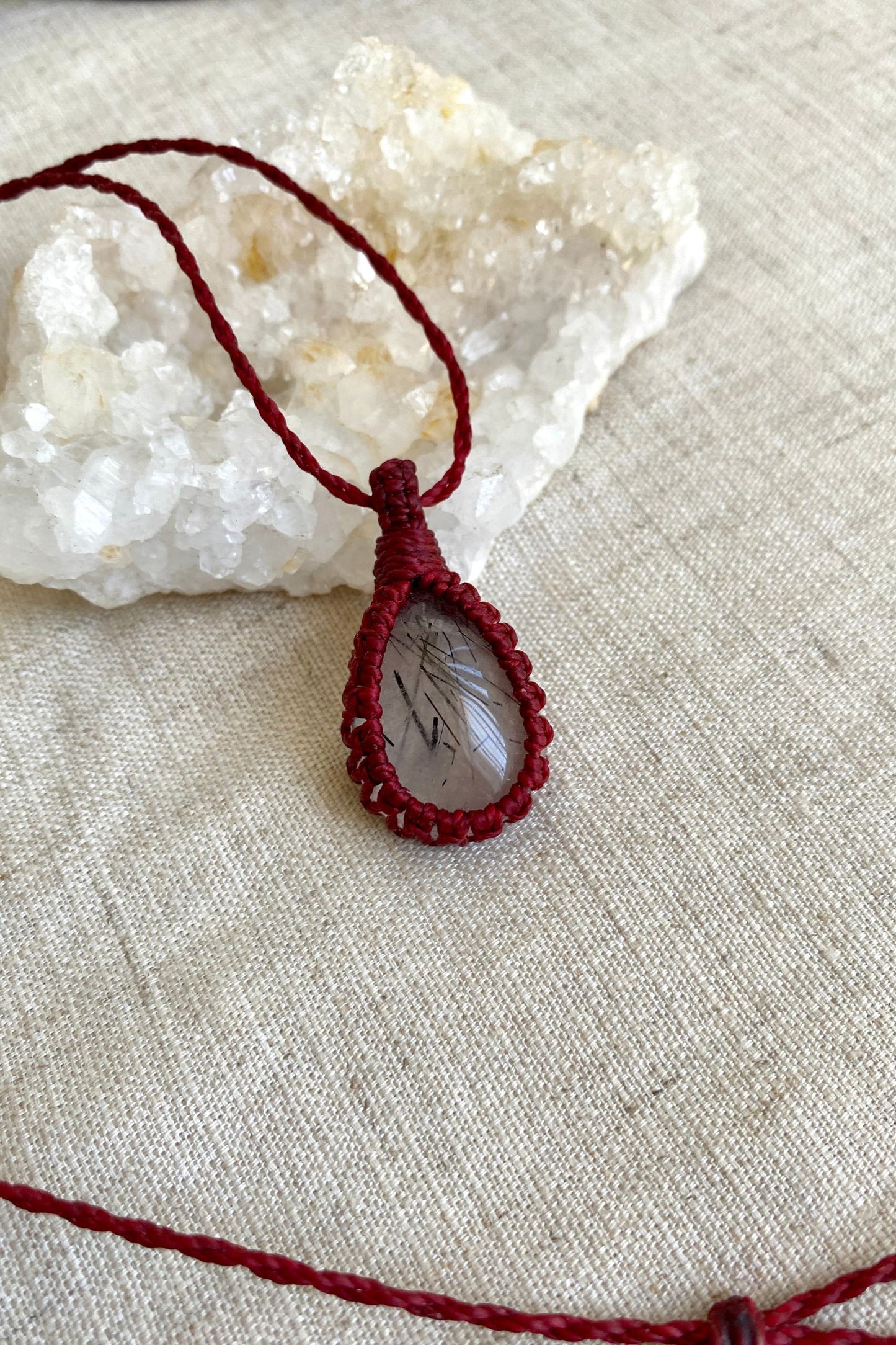 Detailed close-up of a handmade Tourmaline Quartz macrame necklace, emphasizing the striking contrast between the deep red macrame and the clear quartz gemstone.