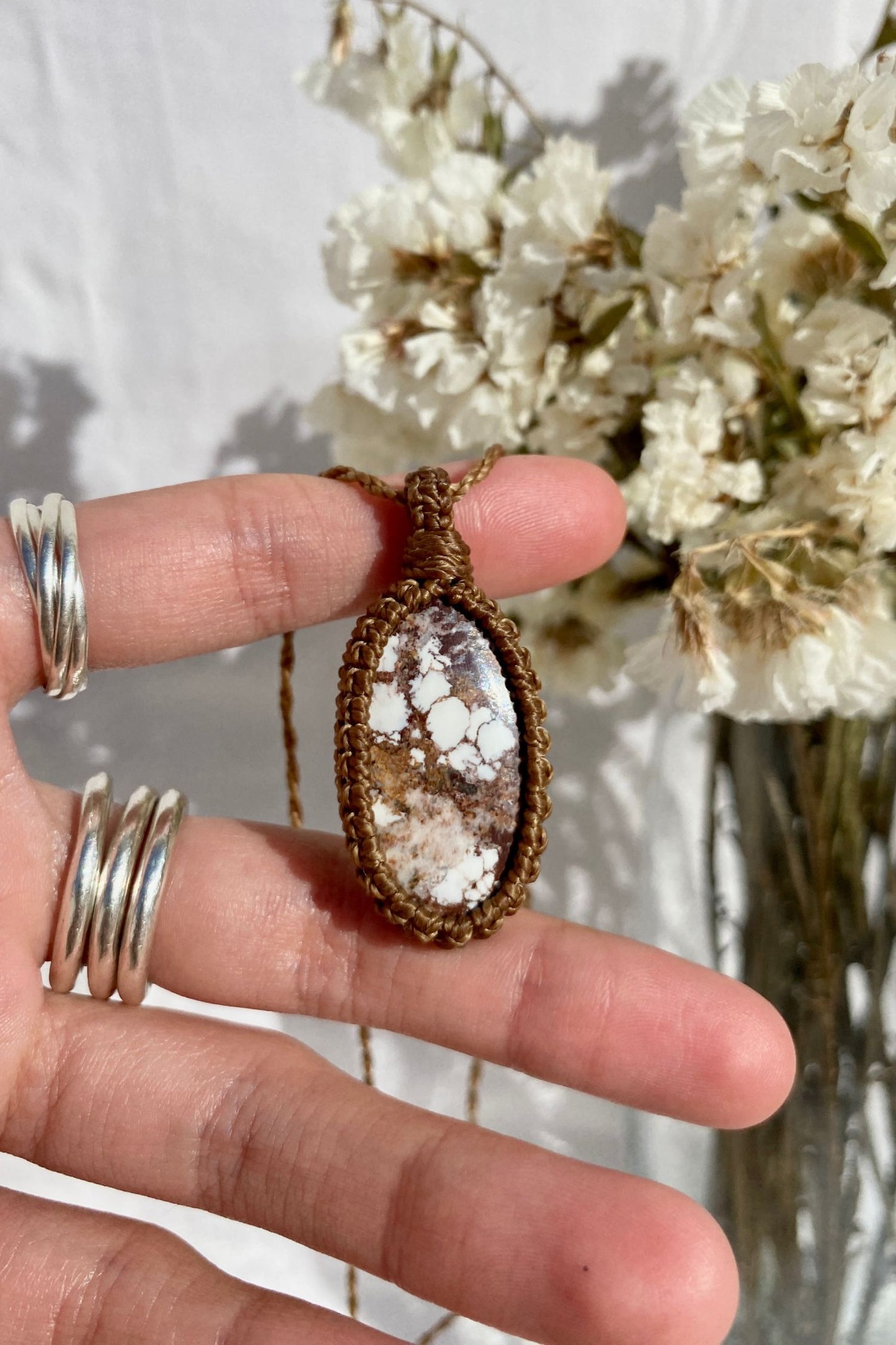 Hand holding a delicate handmade Wild Horse Magnesite macrame necklace, showcasing its unique natural patterns in earthy tones.
