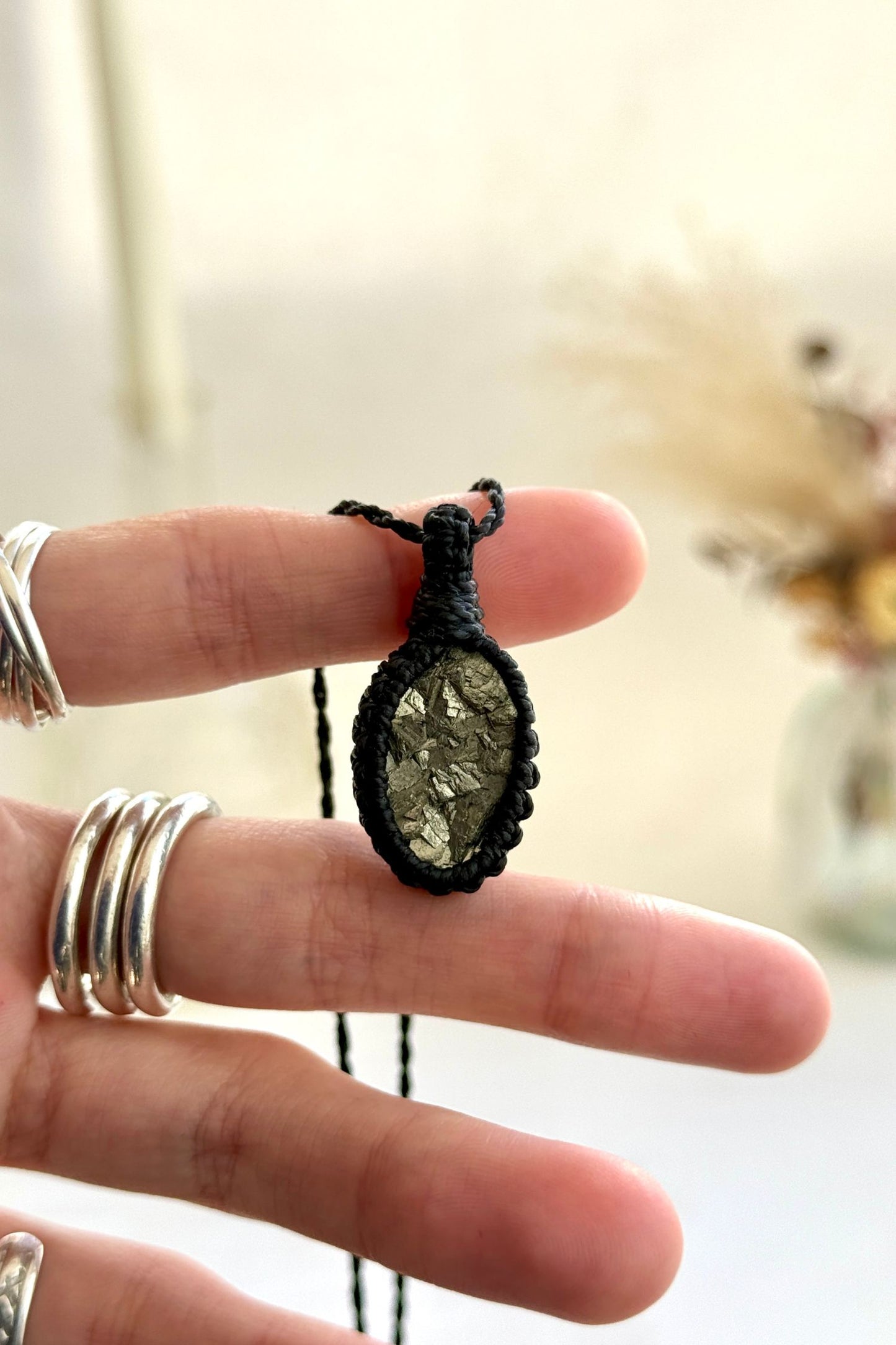 Hand holding a handmade Raw Pyrite macrame necklace with a black cord, showcasing the gemstone's raw beauty with its natural metallic sparkle.