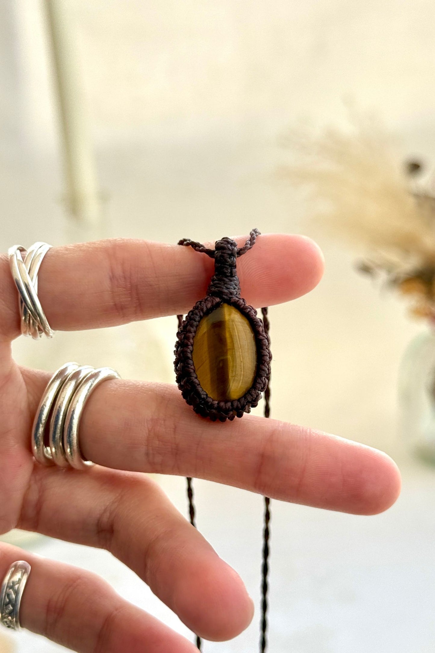 Hand holding a handmade Tiger’s Eye macrame necklace with a brown cord, showcasing the gemstone's rich golden-brown hues.