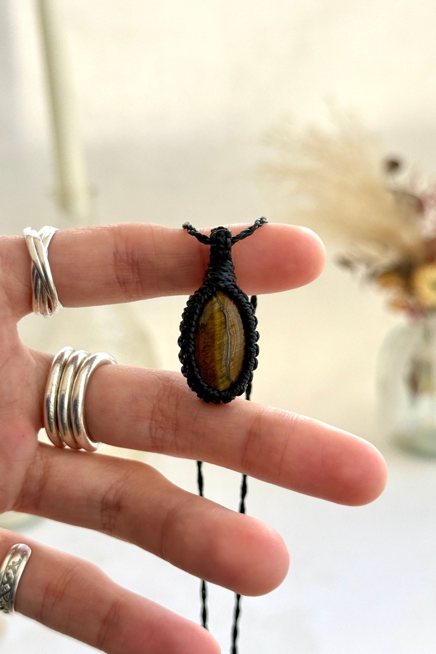 Hand holding a handmade Tiger’s Eye macrame necklace with a black cord, showcasing the gemstone's rich golden-brown hues.
