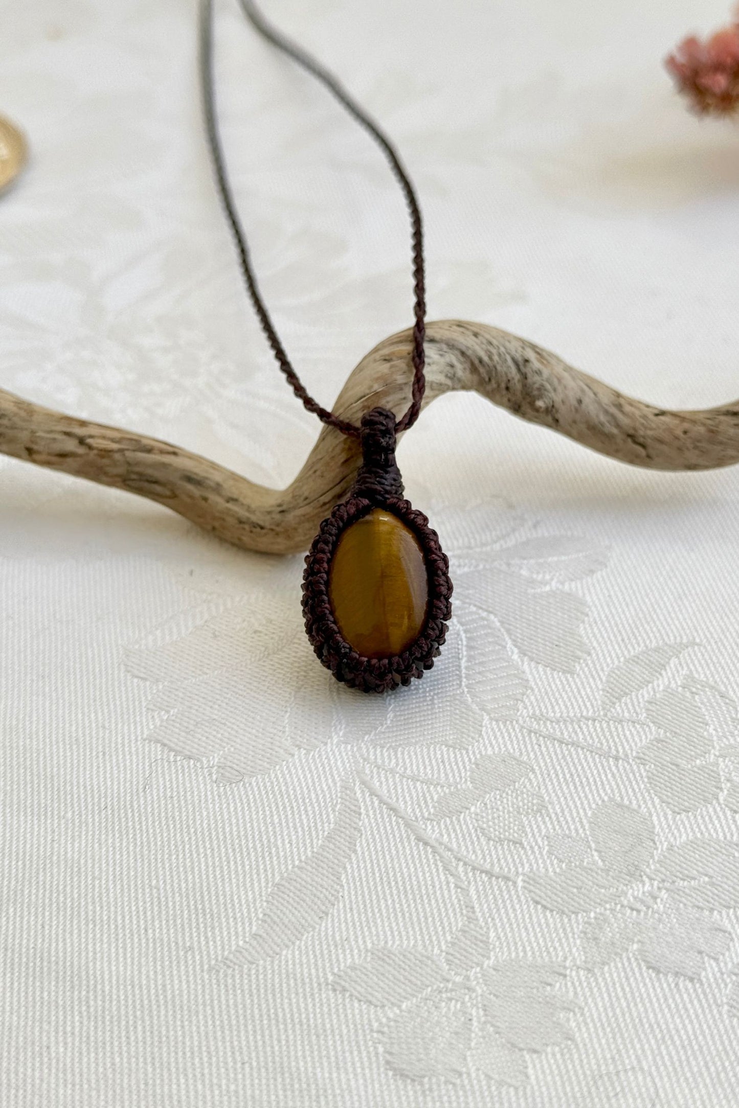 Handmade Tiger’s Eye macrame necklace with a brown cord, laid flat to display its intricate design and glowing gemstone.