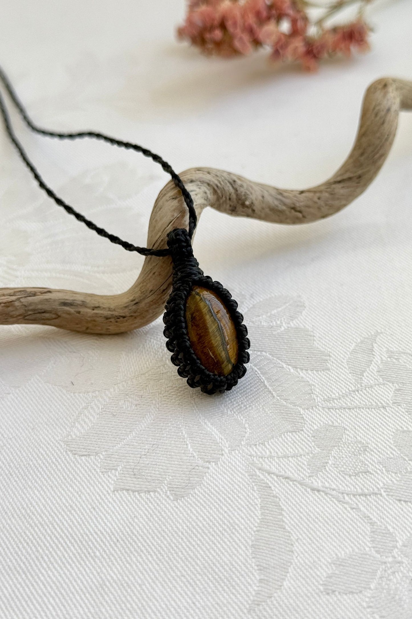 Side view of a Tiger’s Eye macrame necklace wrapped in black cord, highlighting its elegant craftsmanship.