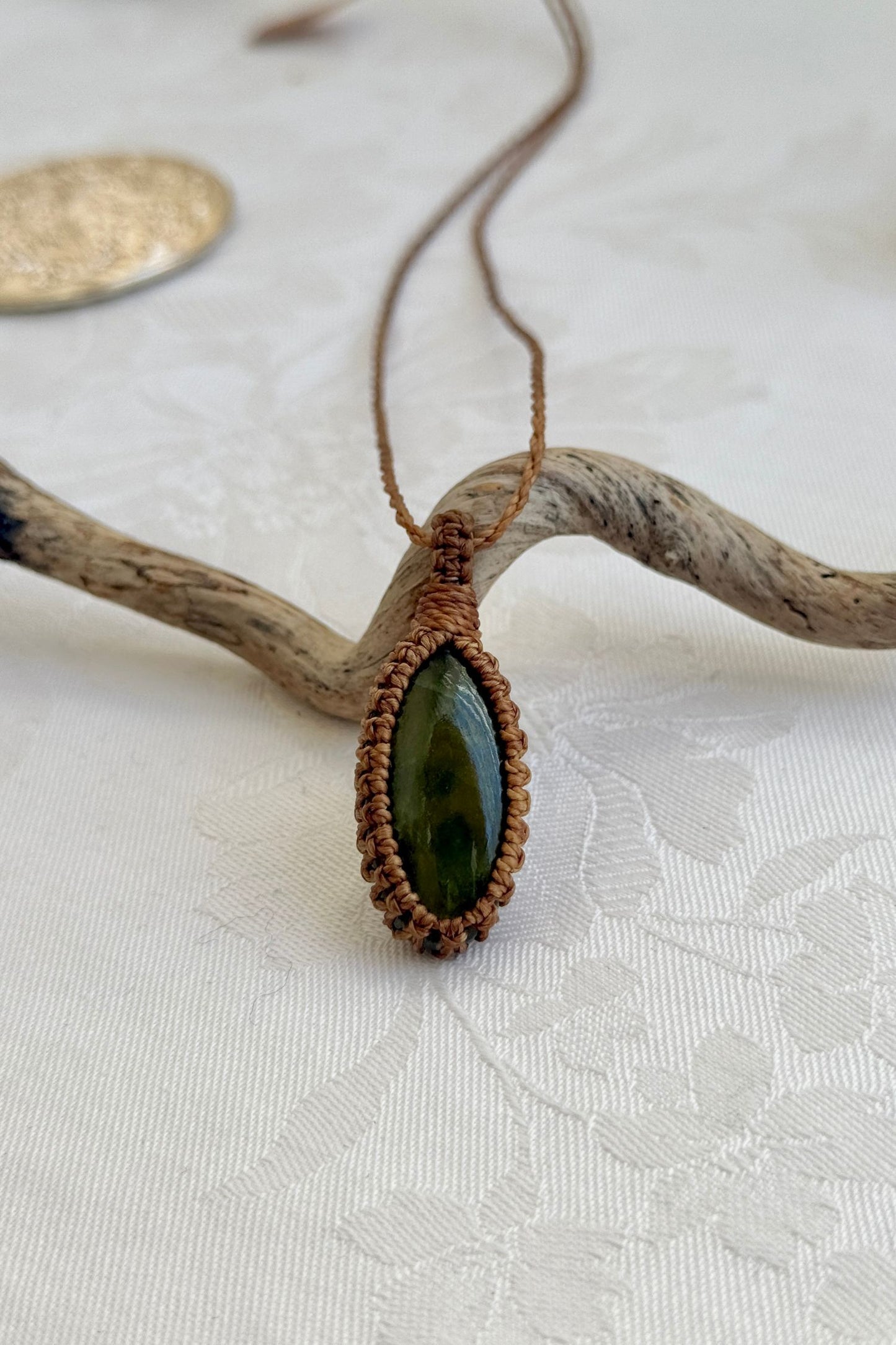 Handmade Vesuvianite macrame necklace with a blue cord, laid flat to display its intricate design and glowing gemstone.