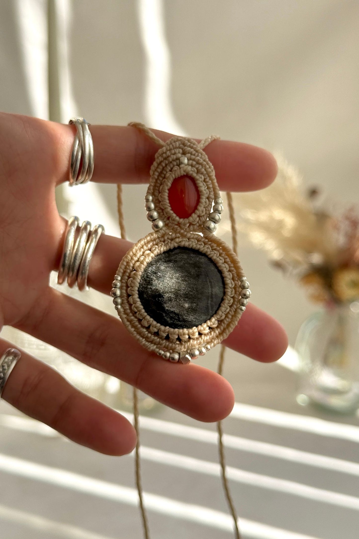 Hand holding a handmade Carnelian and Silver Sheen Obsidian necklace, highlighting the intricate macrame work and the natural glow of the gemstones.
