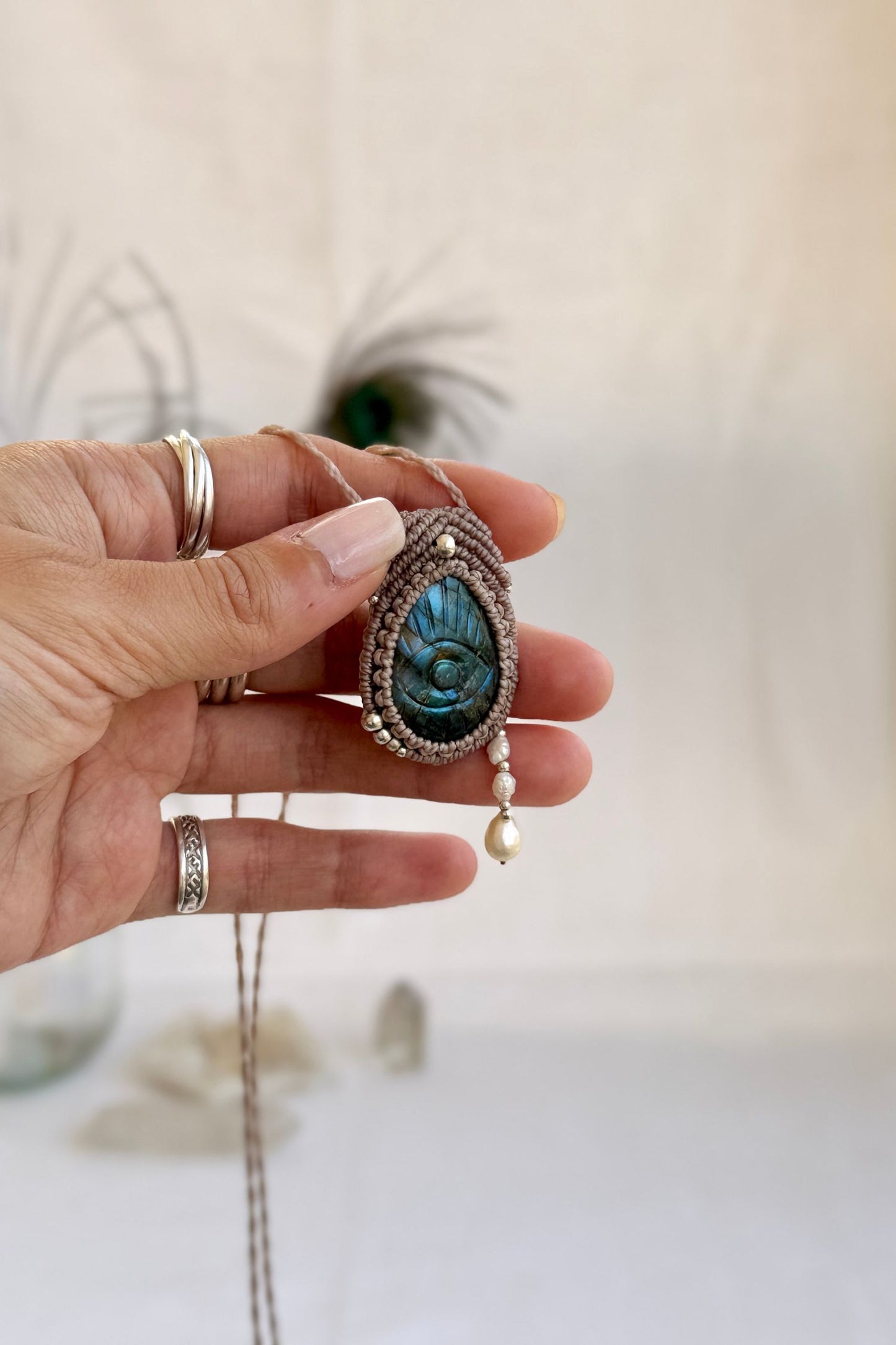 Hand holding handmade Labradorite macrame necklace with dangling fresh water pearl tears, showing the scale and carved gemstone details.