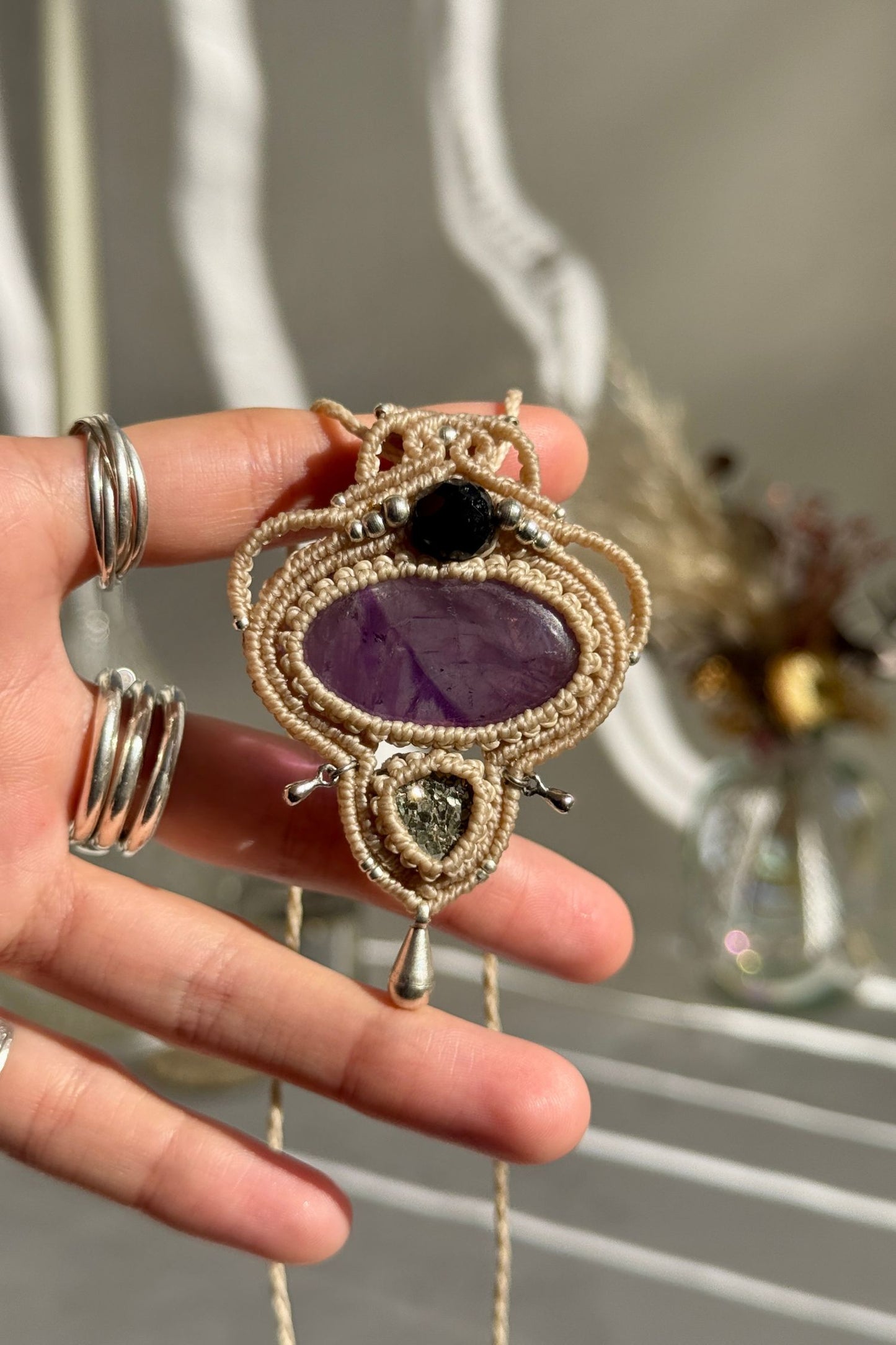 Hand holding a handmade Amethyst and Raw Druzy Pyrite necklace, highlighting the intricate macrame work and the natural glow of the gemstones.