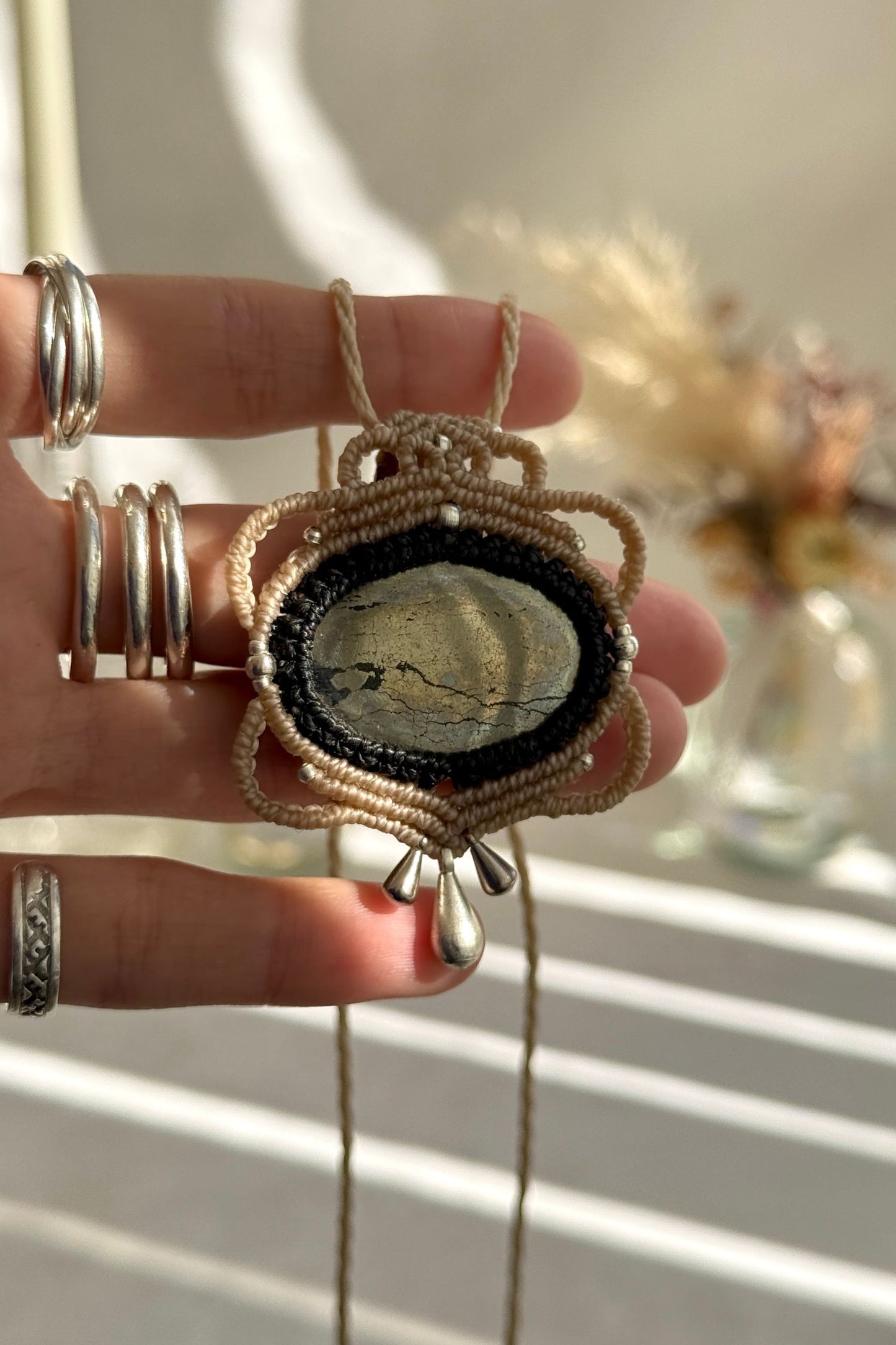 Hand holding a handmade Pyrite necklace, highlighting the intricate macrame work and the natural mirror-like silver of the gemstone.