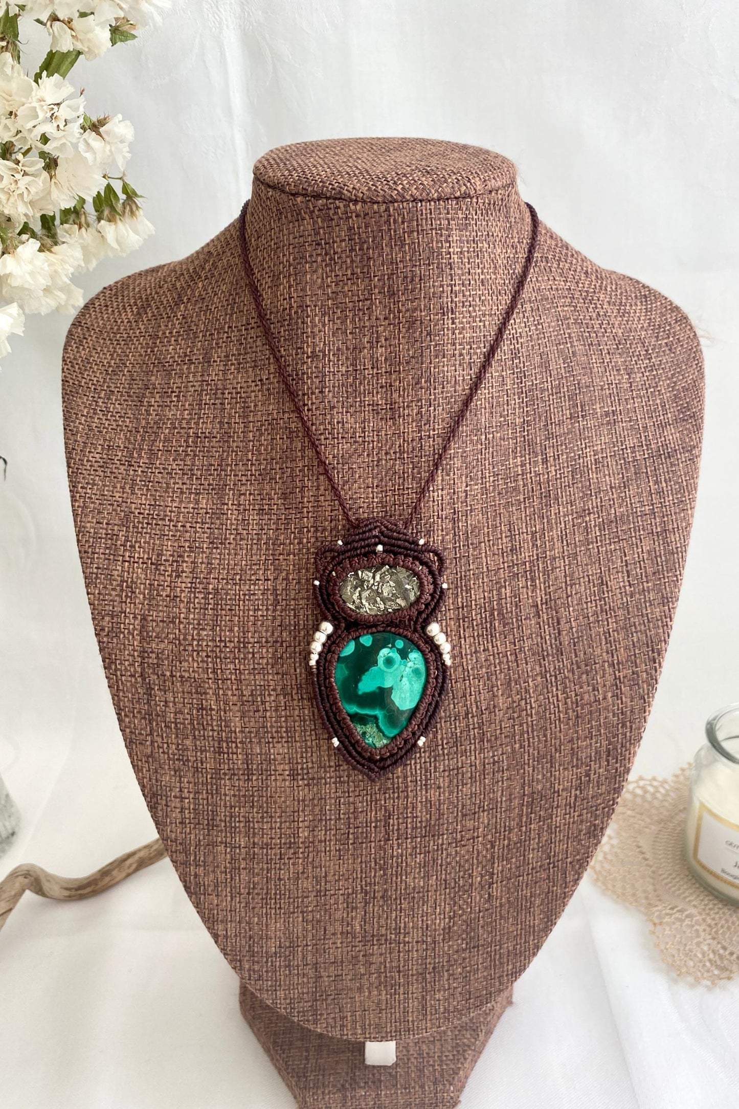 Handmade macrame necklace featuring malachite and raw pyrite displayed on a necklace stand, giving an overview of the piece’s size and design.