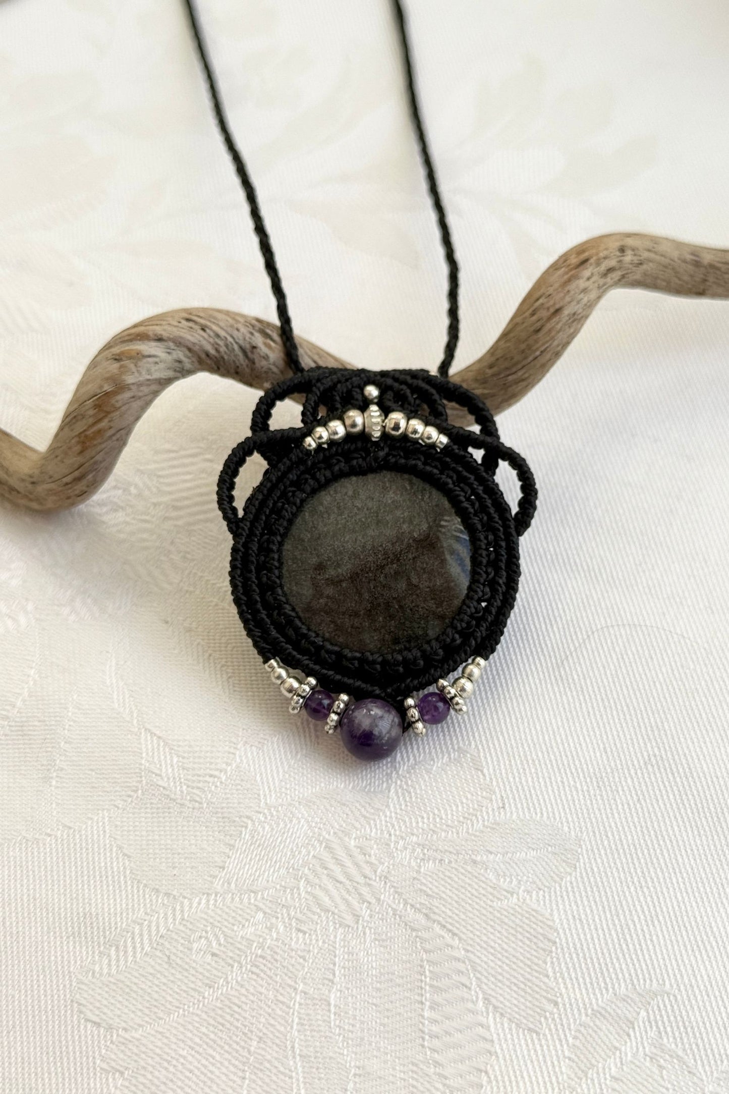 Close-up of the Silver Sheen Obsidian and Amethyst macrame necklace in a unique setting. Highlighting the craftsmanship and gemstones details.
