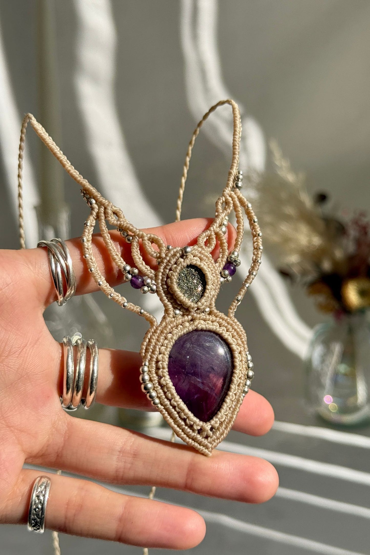 Hand holding a handmade Amethyst and Druzy Pyrite necklace, highlighting the intricate macrame work and the natural glow of the gemstones.