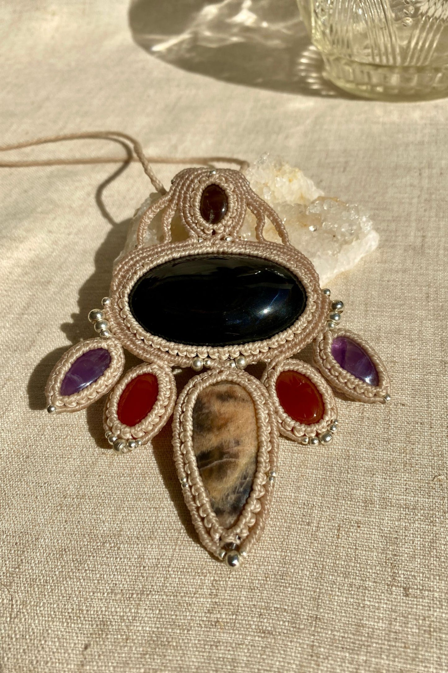 Handmade multi-gemstone macrame necklace laid flat, showcasing the intricate design and gemstones—obsidian, black moonstone, smoky quartz, carnelian, and amethyst—on a clean background.