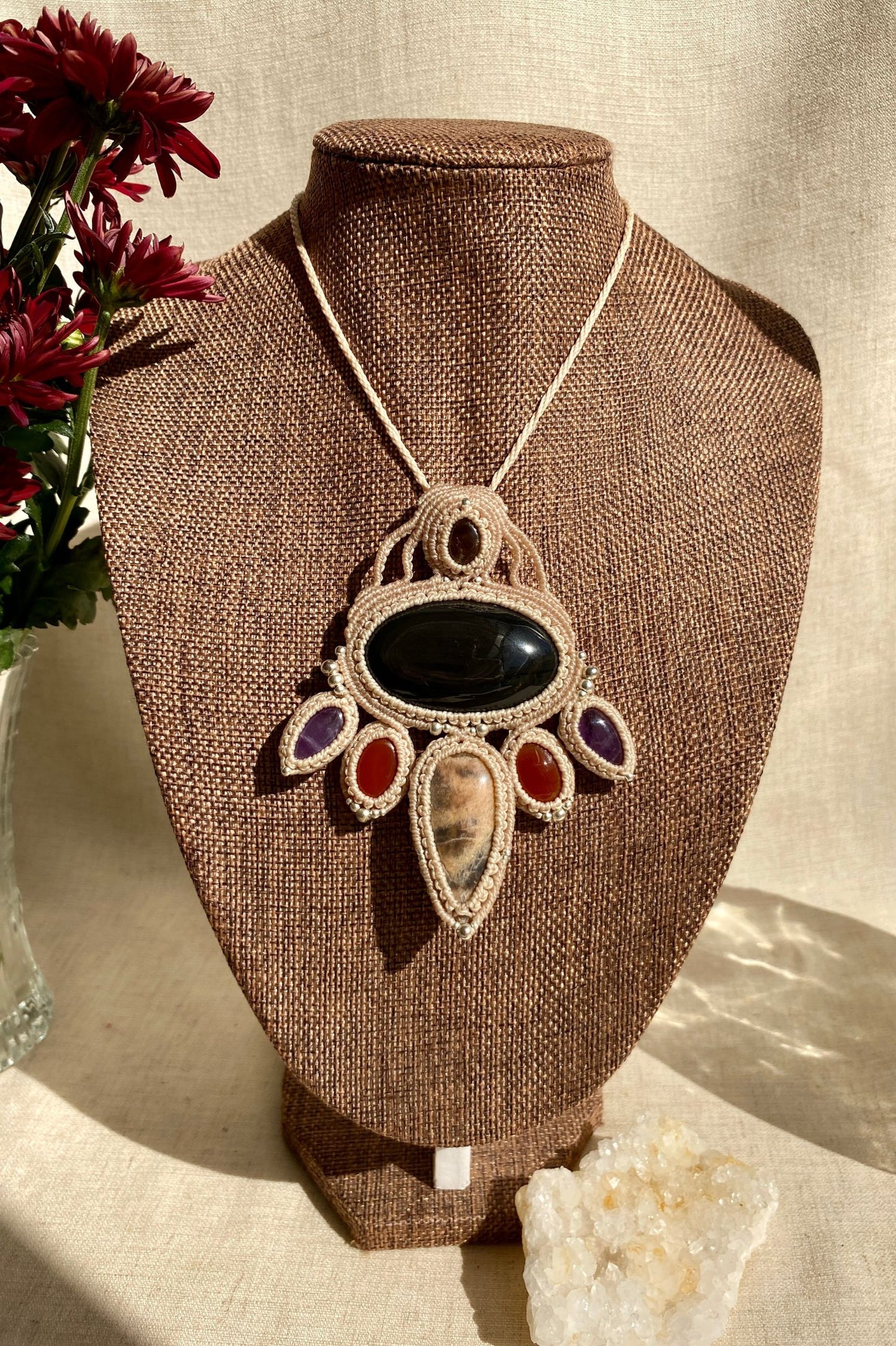 Handmade macrame necklace featuring obsidian, black moonstone, smoky quartz, carnelian, and amethyst, displayed on a necklace stand to show how it drapes.