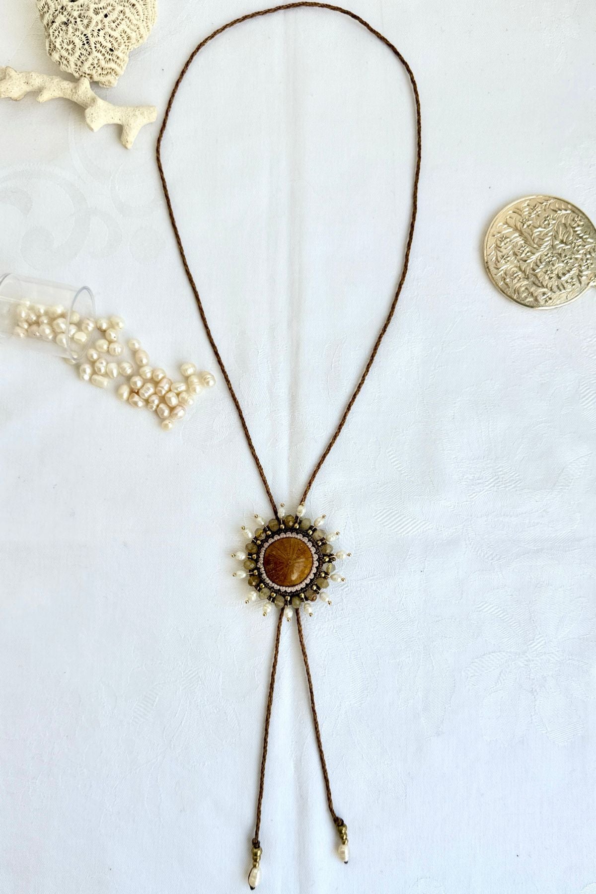 Complete sea urchin fossil bolo tie laid flat with pearls and coral fossils, showing full adjustable design and central gemstone details