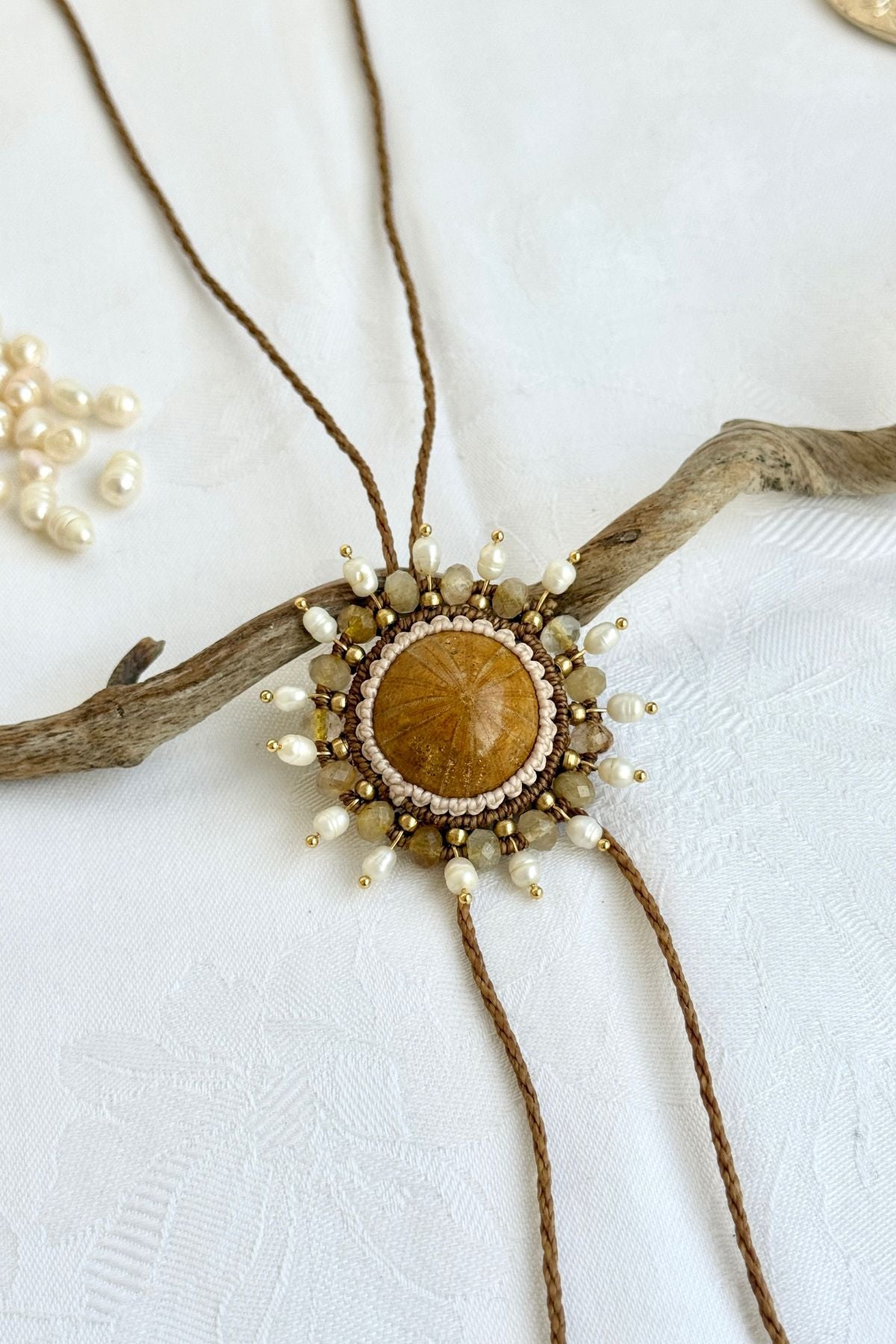 Macro view of sea urchin fossil bolo tie highlighting rutilated quartz, freshwater pearls, and intricate artisan macramé design