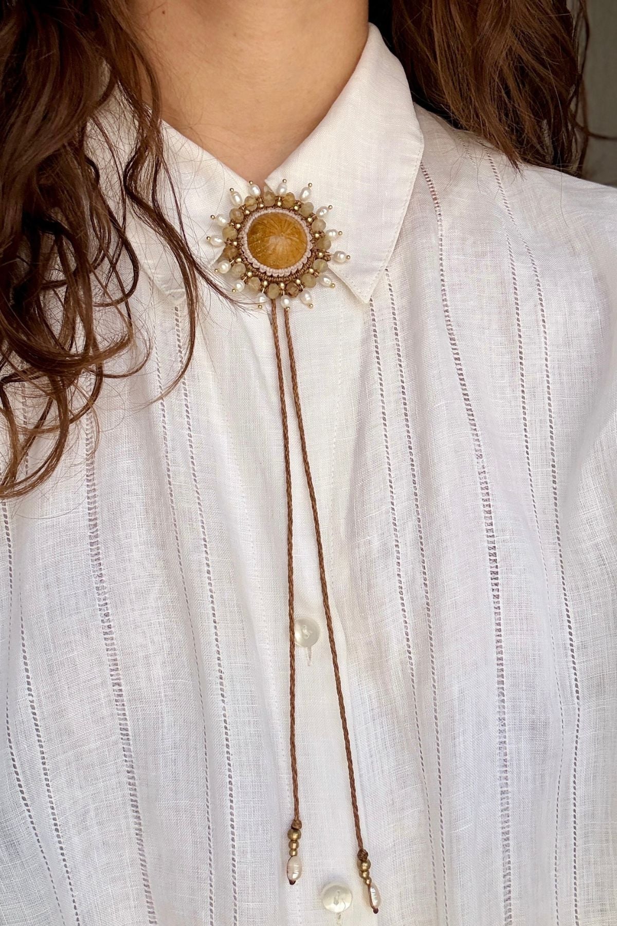 Model wearing sea urchin fossil bolo tie at shirt collar, showcasing full statement accessory in an elegant outfit