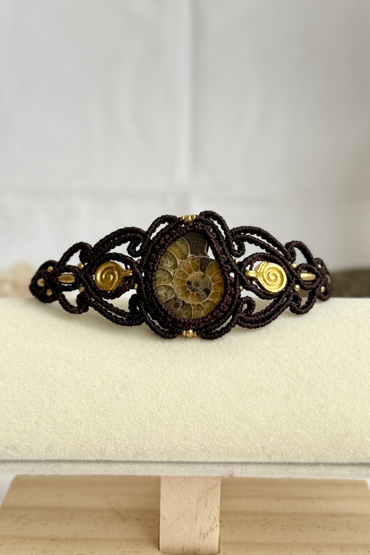 Yellow ammonite cuff bracelet displayed flat, highlighting spiral brass details and earthy brown cord contrast