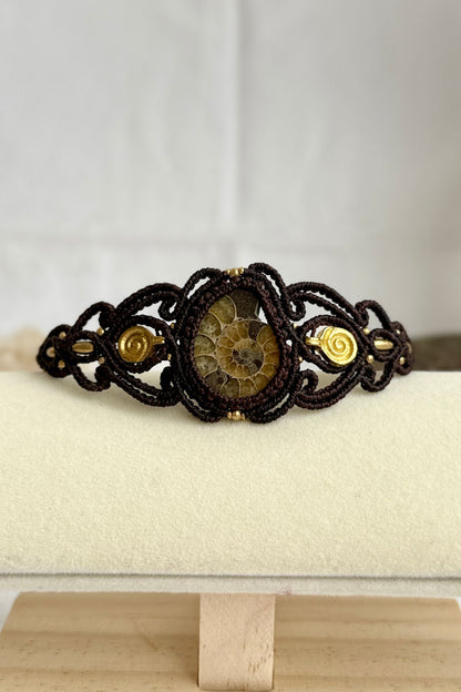 Yellow ammonite cuff bracelet displayed flat, highlighting spiral brass details and earthy brown cord contrast