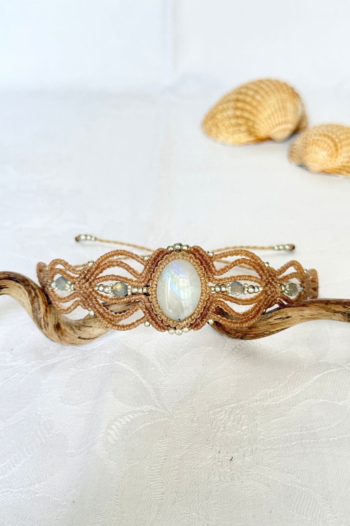 Rainbow Moonstone cuff bracelet with faceted Labradorite beads and openwork beige macrame, displayed on a curved branch.