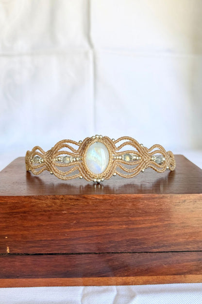 Front view of the macrame cuff bracelet on a wooden box, with a blue flash across the central Rainbow Moonstone.