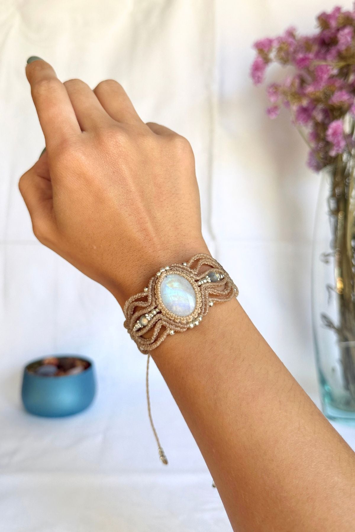 Macrame cuff bracelet worn on a wrist, showing the iridescent Rainbow Moonstone and Labradorite beads on either side.