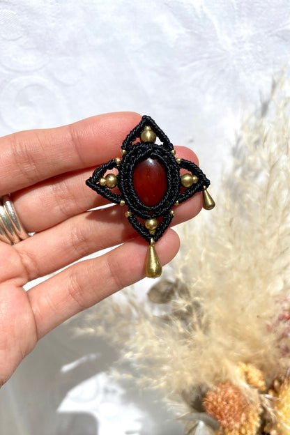Handmade statement brooch with a deep red Carnelian gemstone and asymmetrical golden details, held in hand to showcase its size and intricate design.