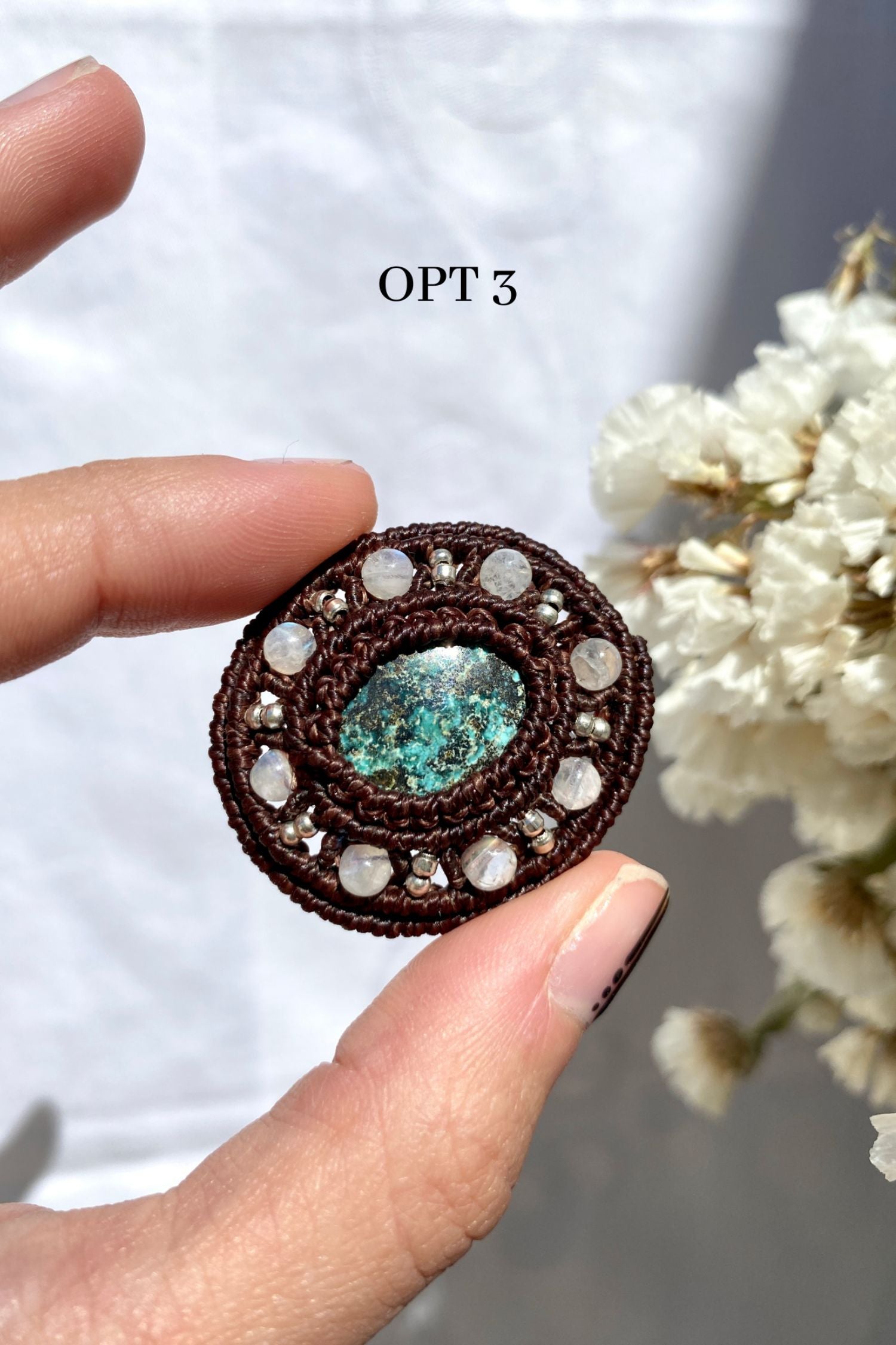Handmade round turquoise brooch being secured in hand, showing its detailed craftsmanship and elegant macrame design.
