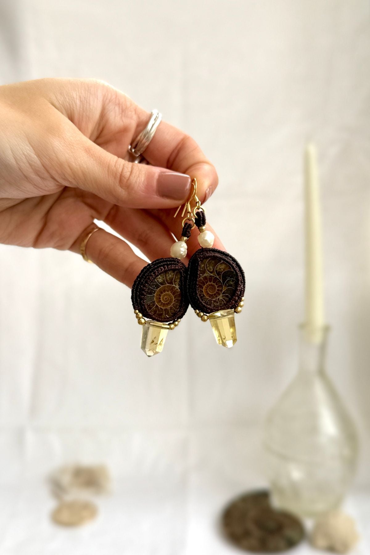 Sliced ammonite statement earrings held in hands, showcasing smoky quartz points, pearl accents, and delicate craftsmanship